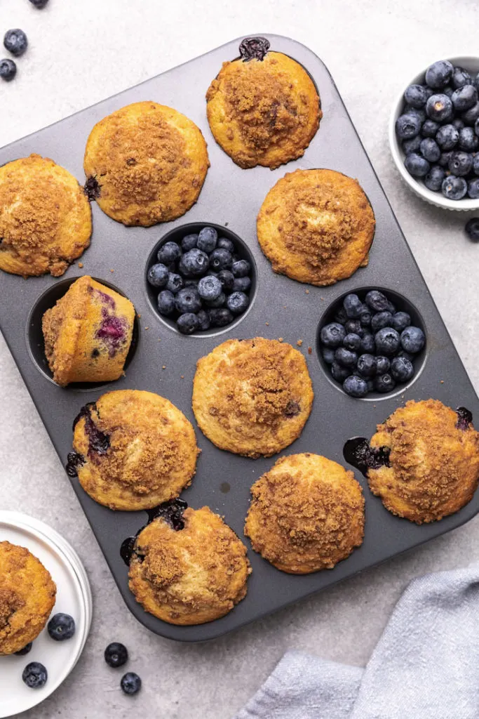 Close up view of muffins and blueberries in a muffin pan.