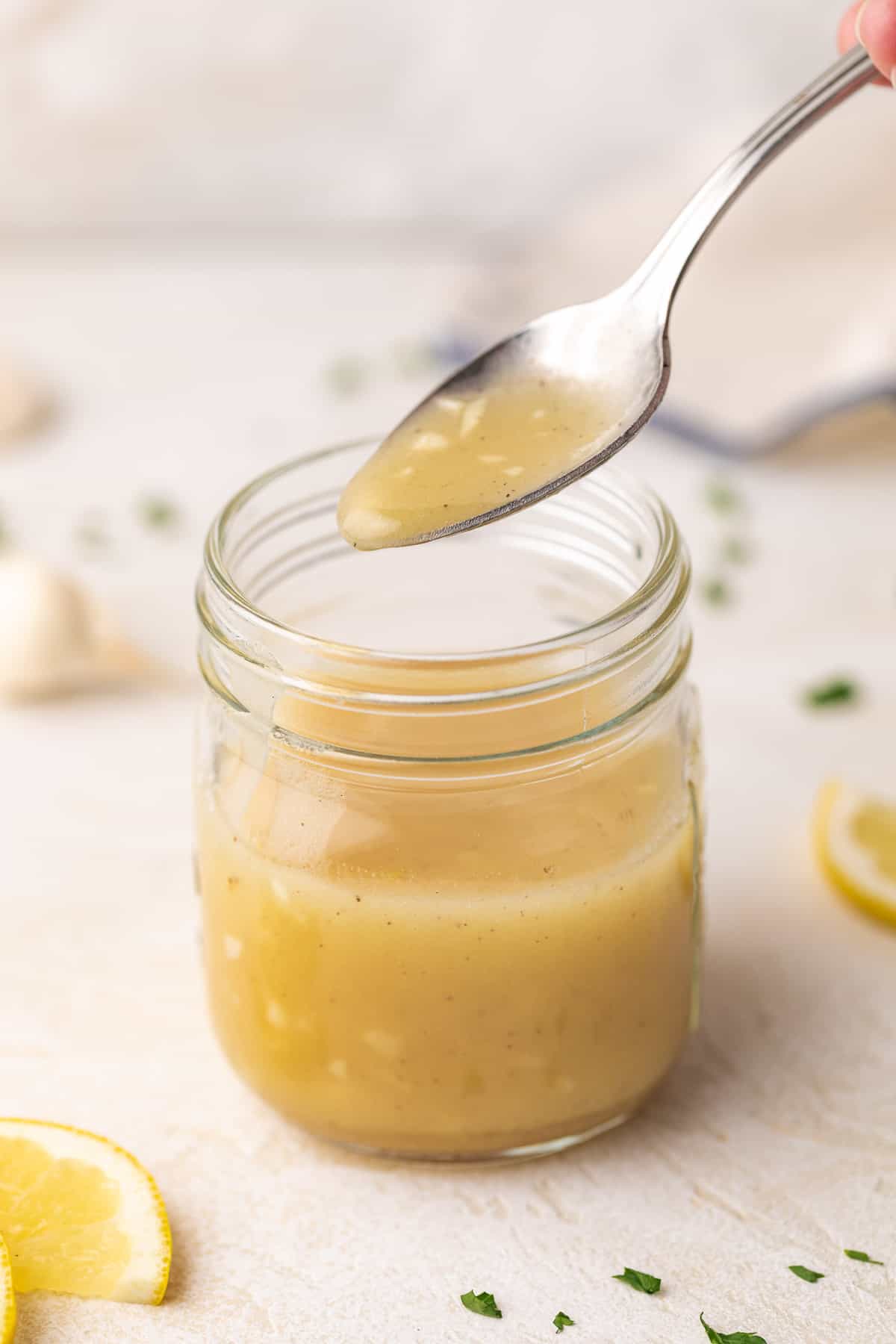 Spoon of salad dressing above a jar.