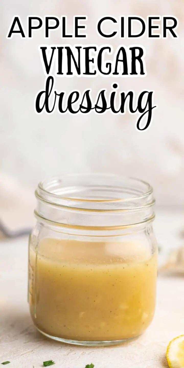 Side view of a jar of tangy salad dressing next to a lemon.