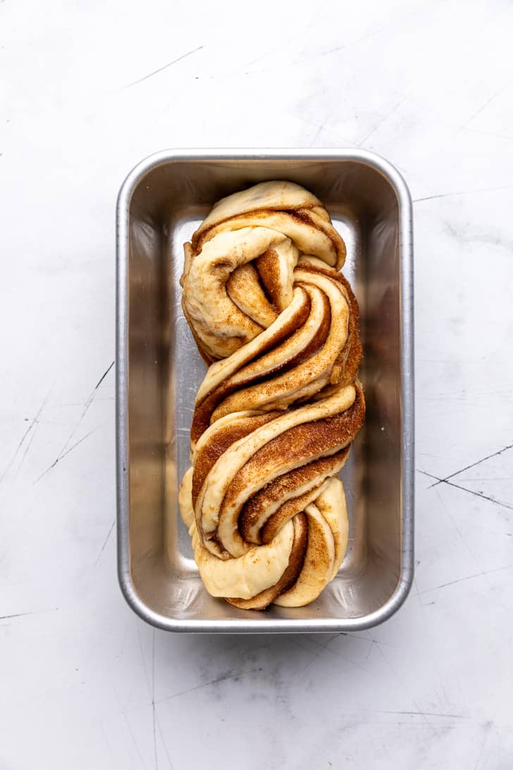 Twisted cinnamon roll dough in a greased loaf pan.