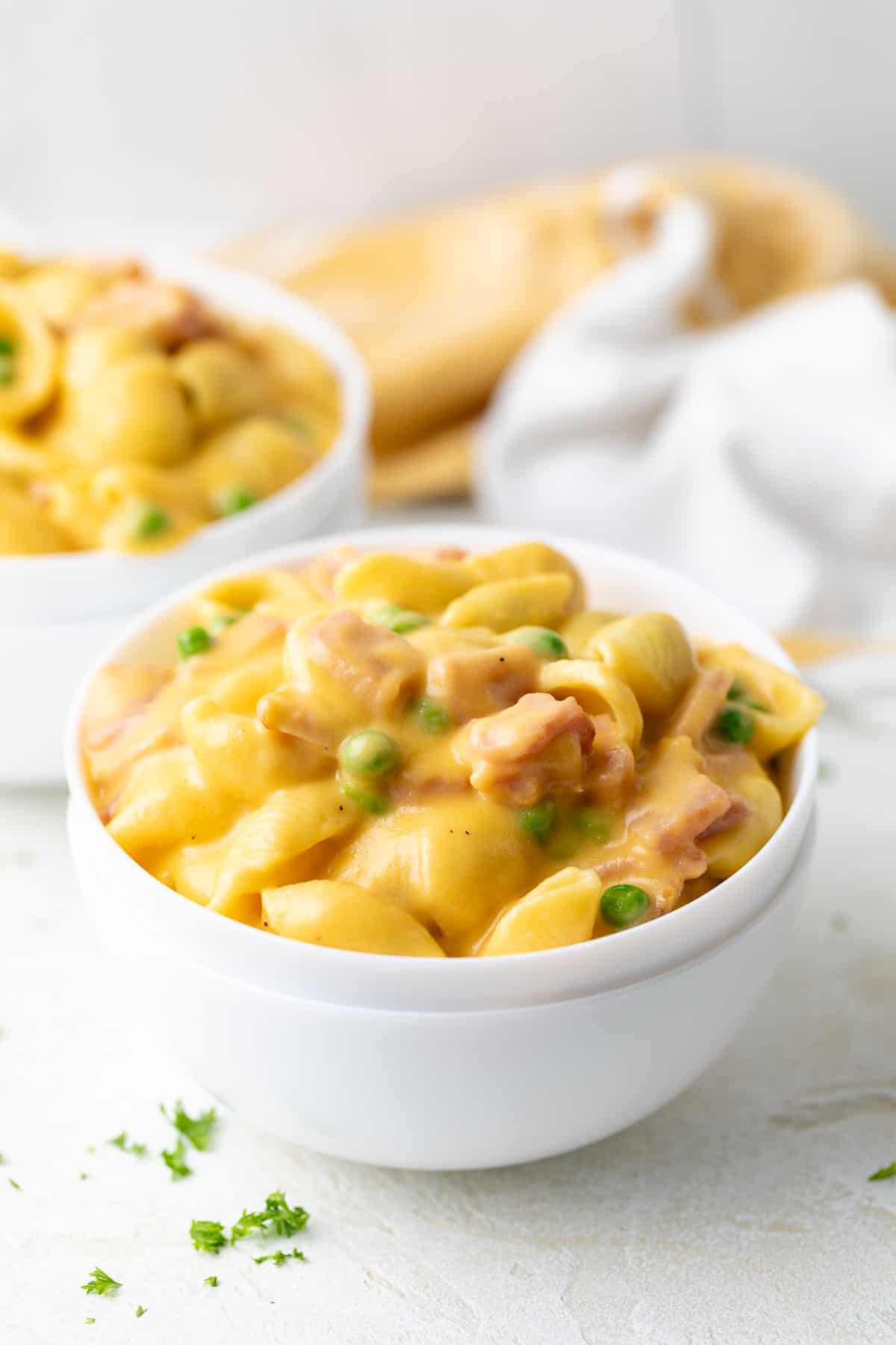 Cheesy pasta with ham and peas in a stack of white bowls.