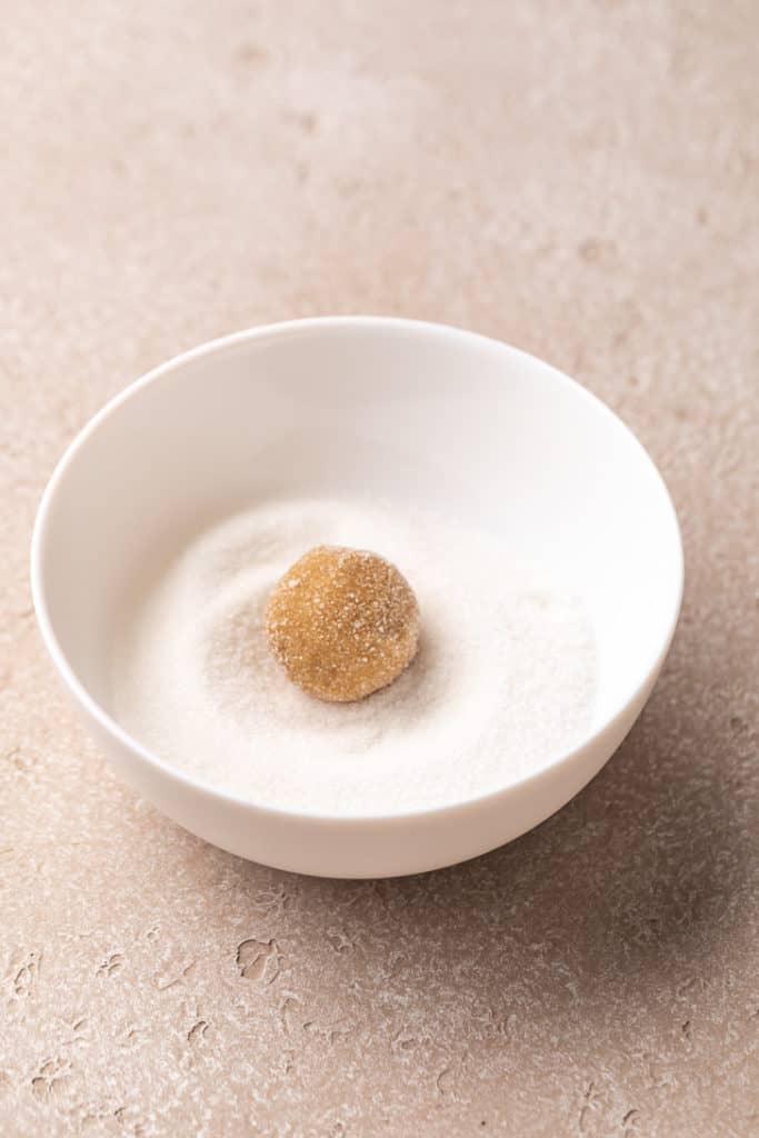 Cookie dough ball in a bowl of granulated sugar.