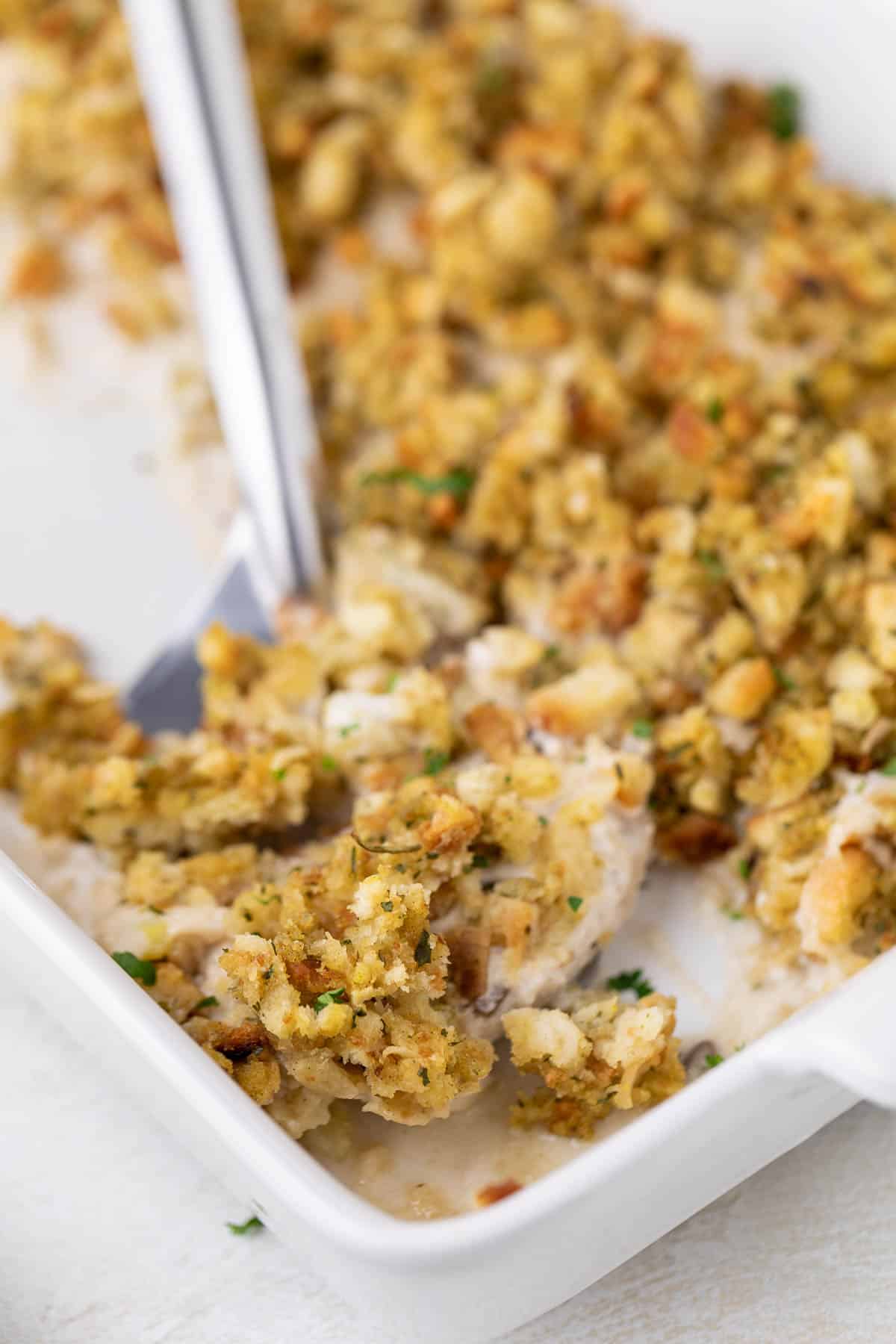 Spatula scooping pork chop and stuffing bake out of a pan.