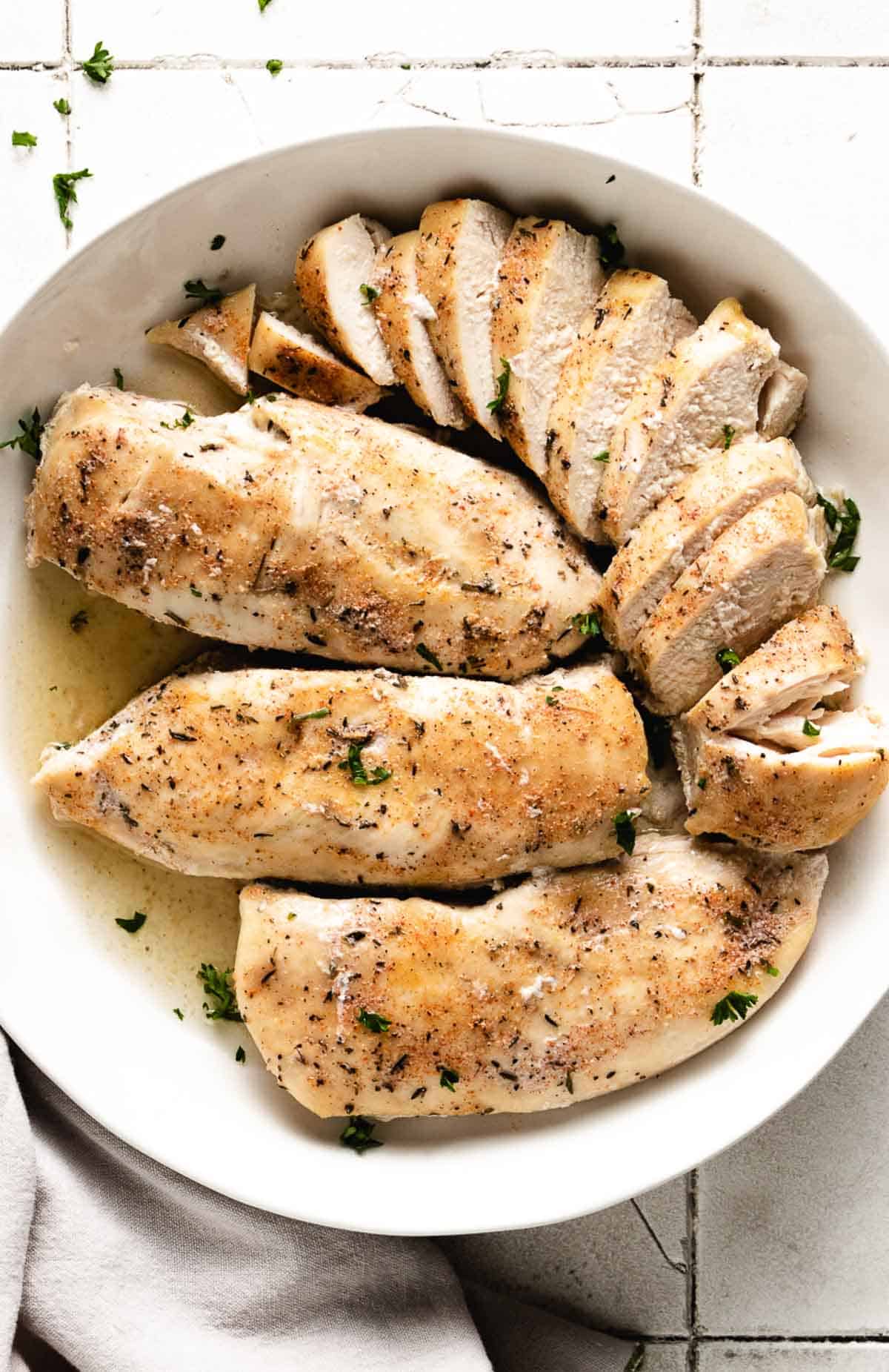 Top down view of four cooked chicken breasts in a dish.