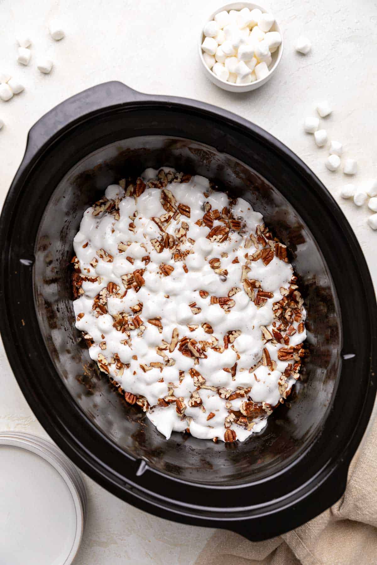 Top down view of melted marshmallows and pecans in a slow cooker.