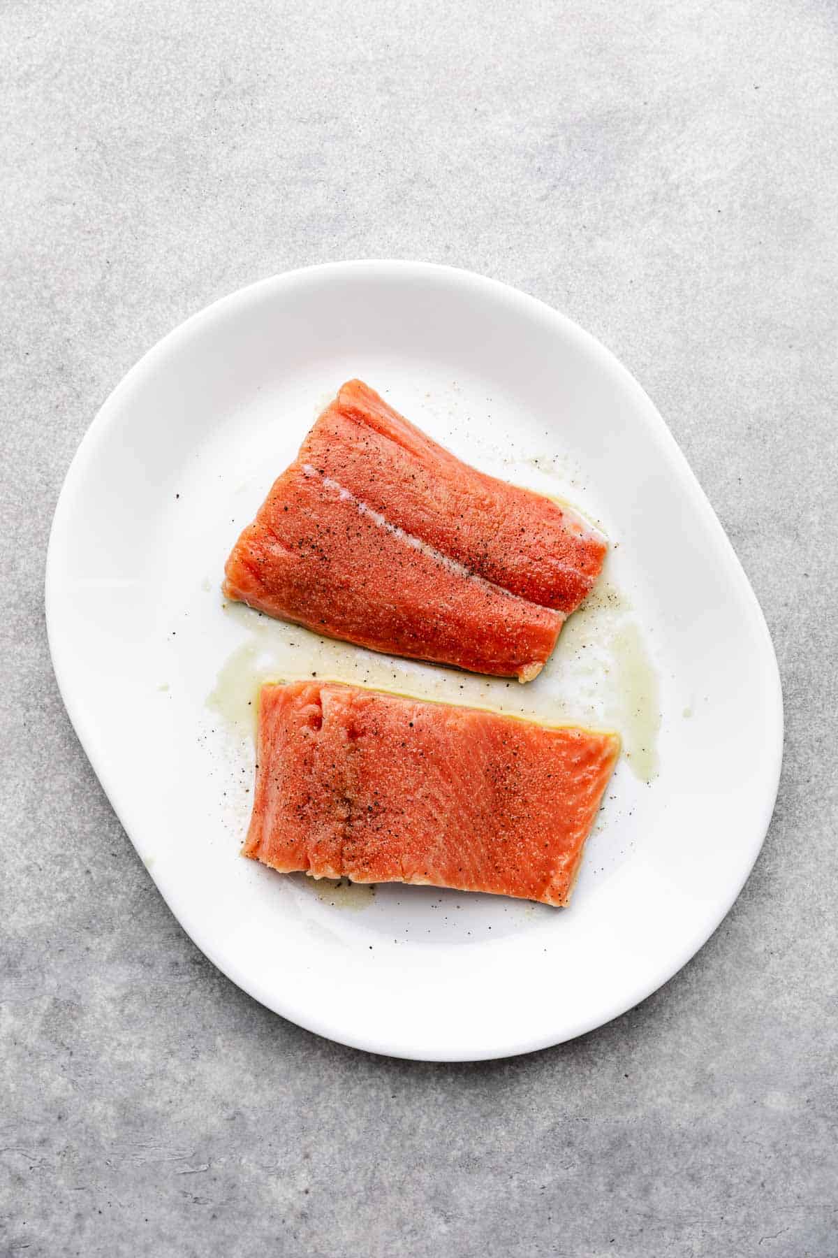 Salt, pepper, and olive oil sprinkled over uncooked salmon.