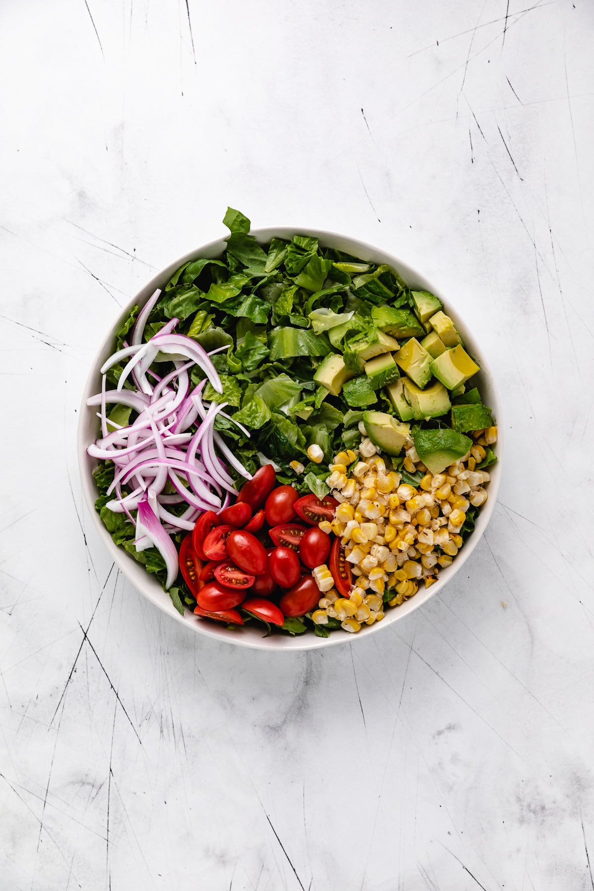 Corn, onions, tomatoes, avocado, and lettuce in a bowl.