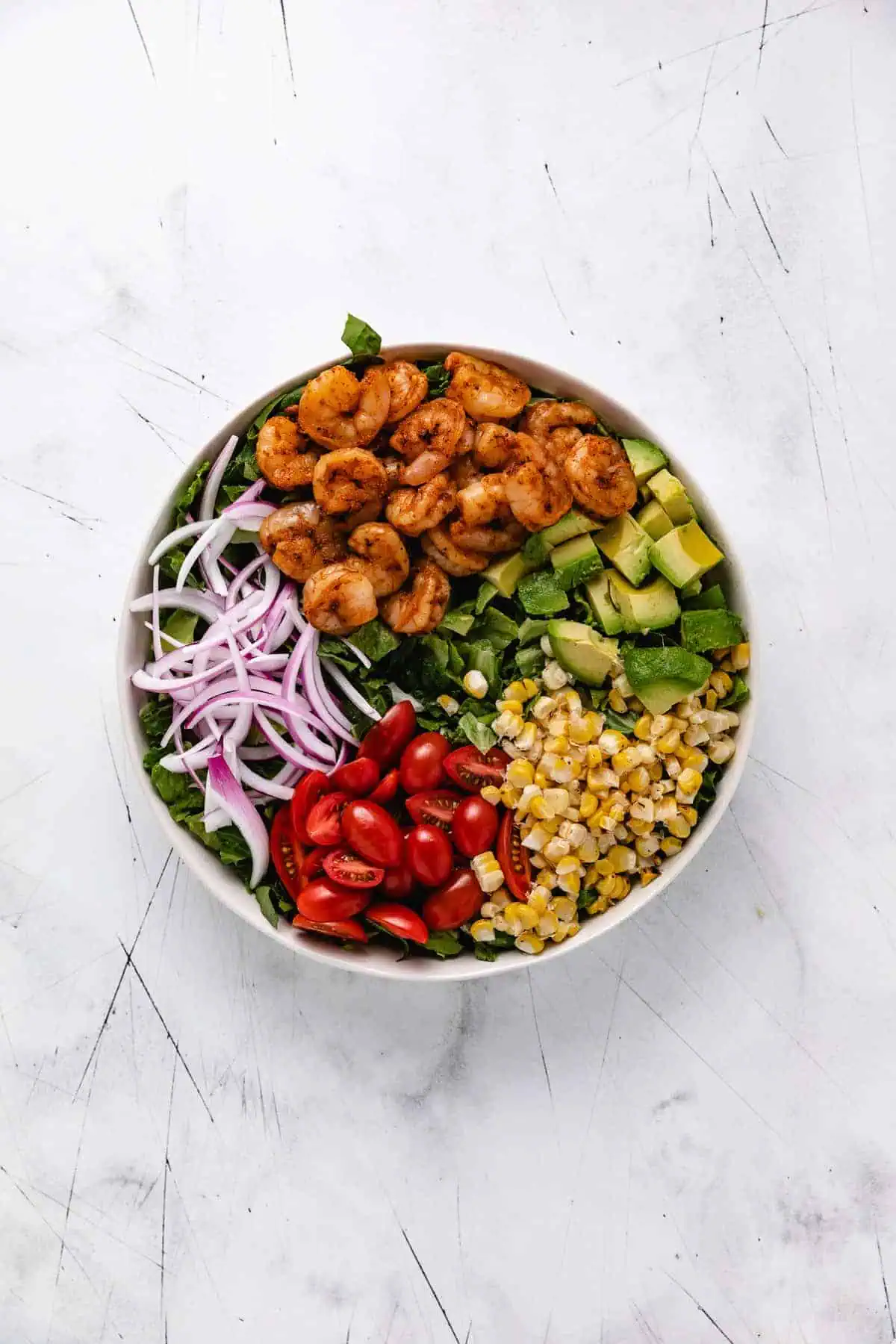 Corn, onions, tomatoes, avocado, shrimp, and lettuce in a bowl.