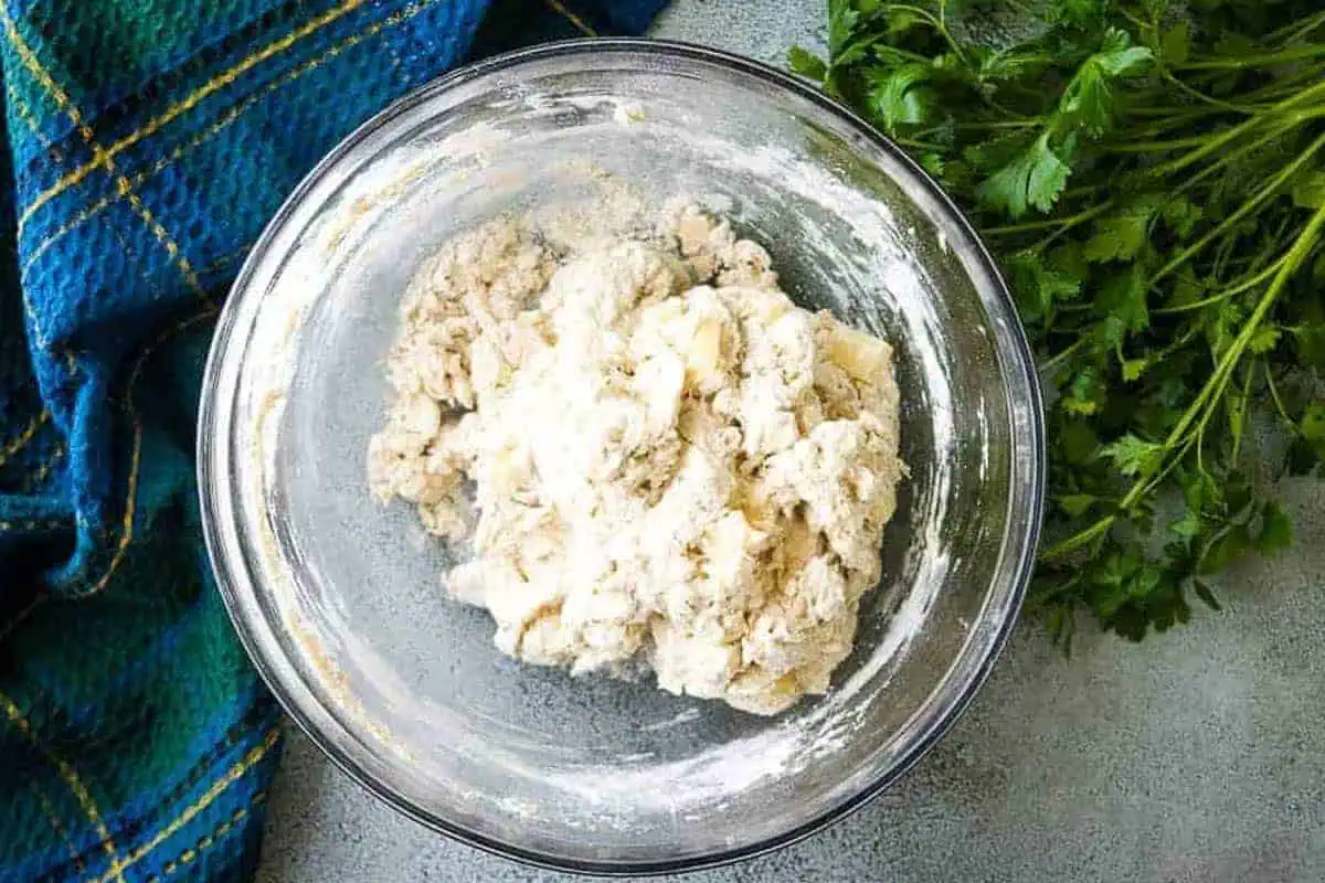 Cheese and rosemary added to a bowl of bread dough.