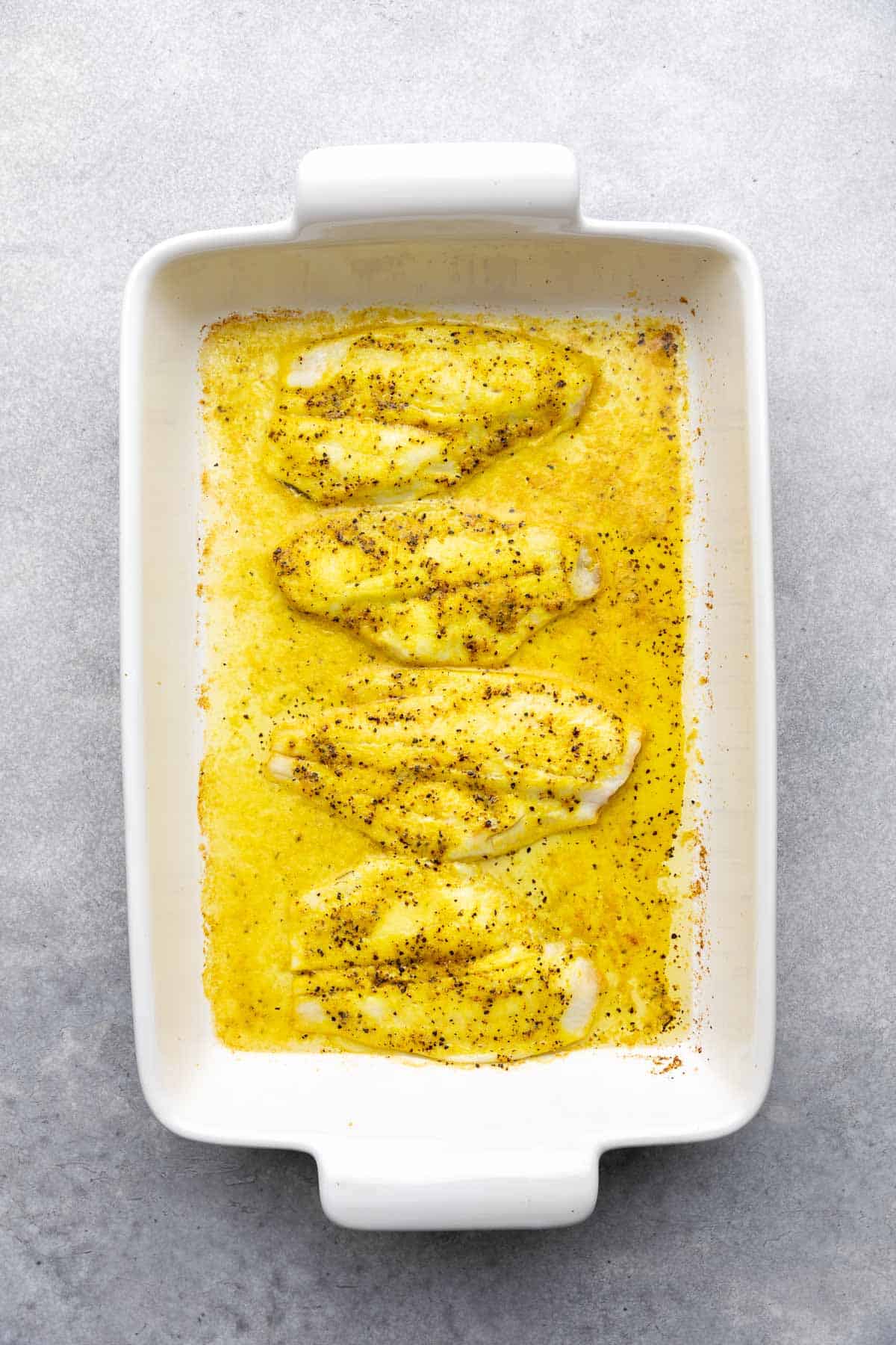 Oven baked lemon pepper flounder in a white baking dish.
