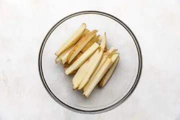 Glass bowl filled with sliced potatoes.