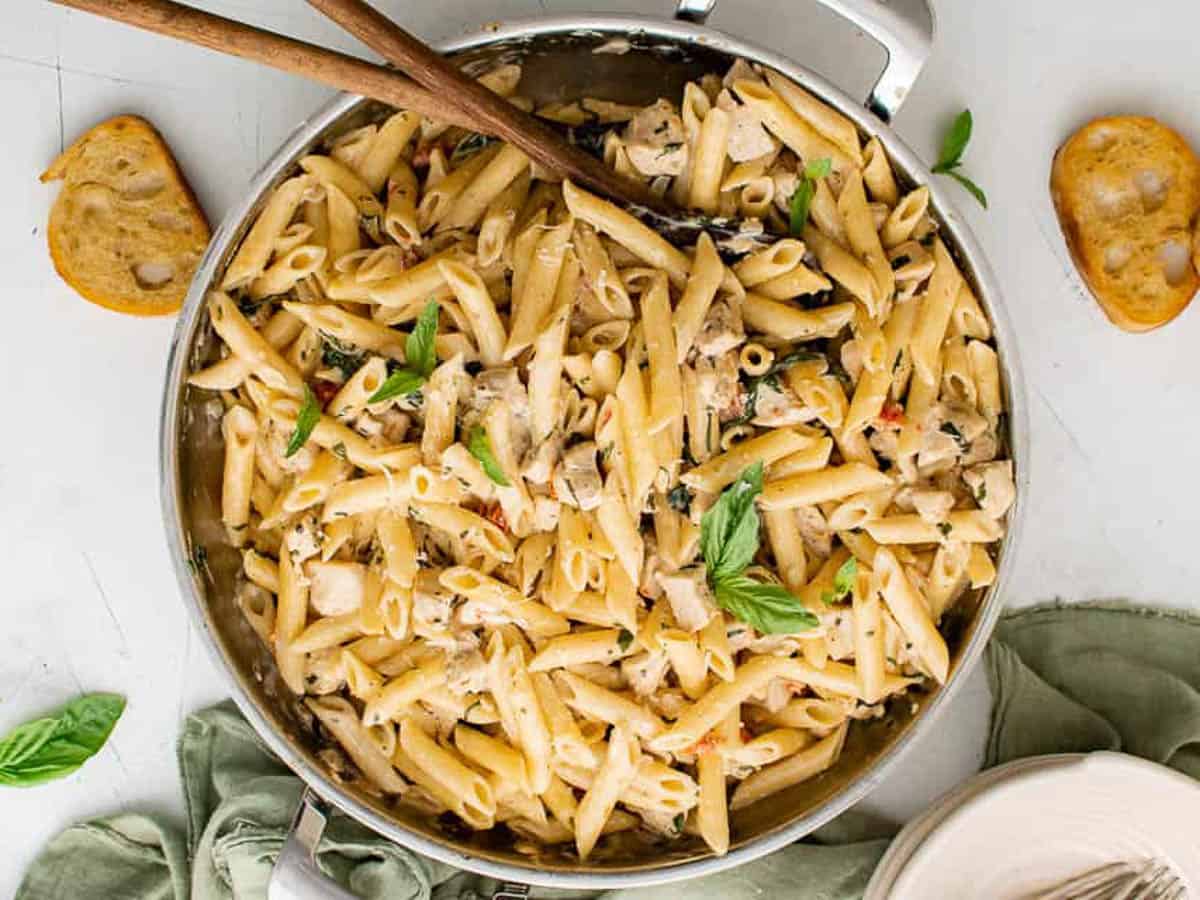 Large pan of tuscan chicken pasta with wooden spoons.