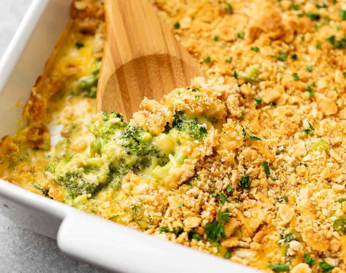 Wooden spoon in a pan of broccoli cheese casserole.