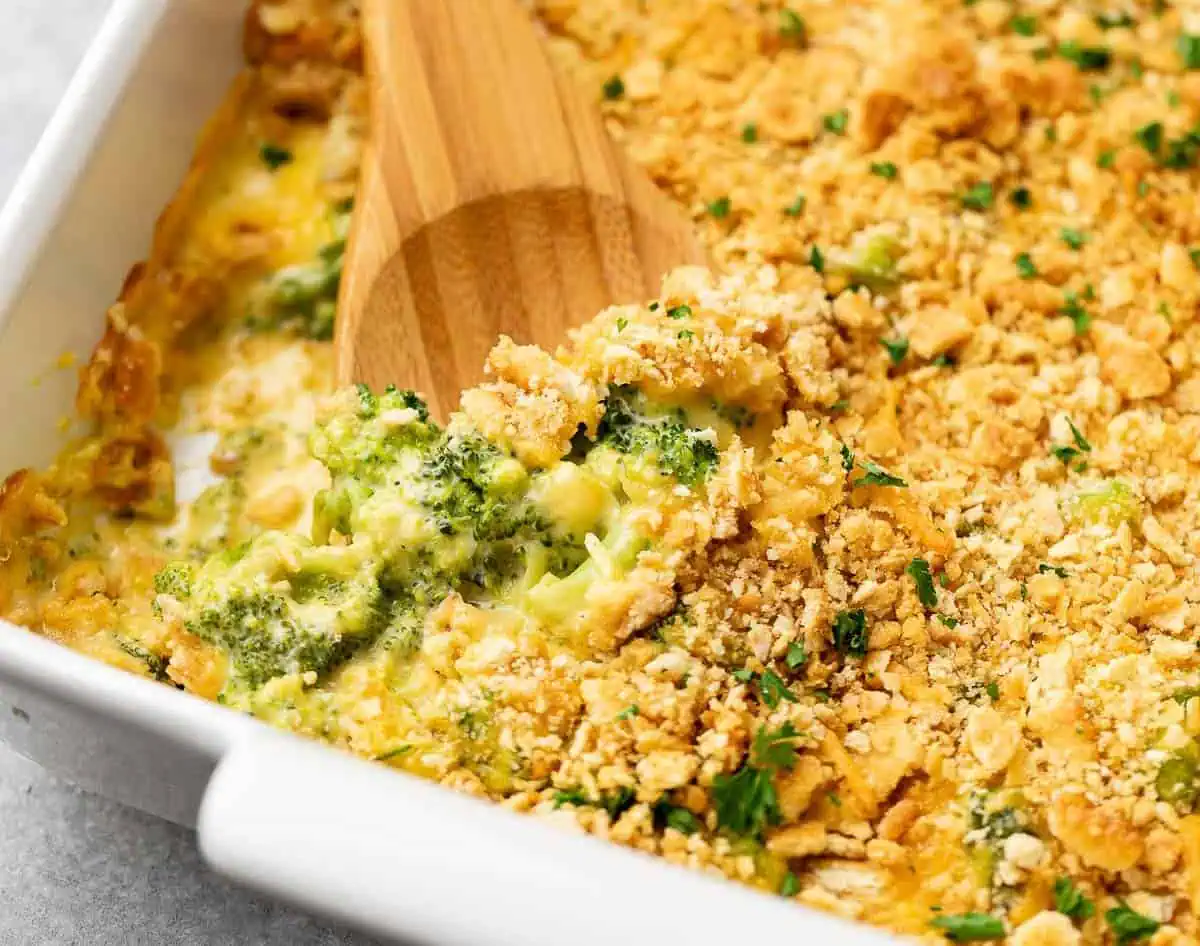 Wooden spoon in a pan of broccoli cheese casserole.