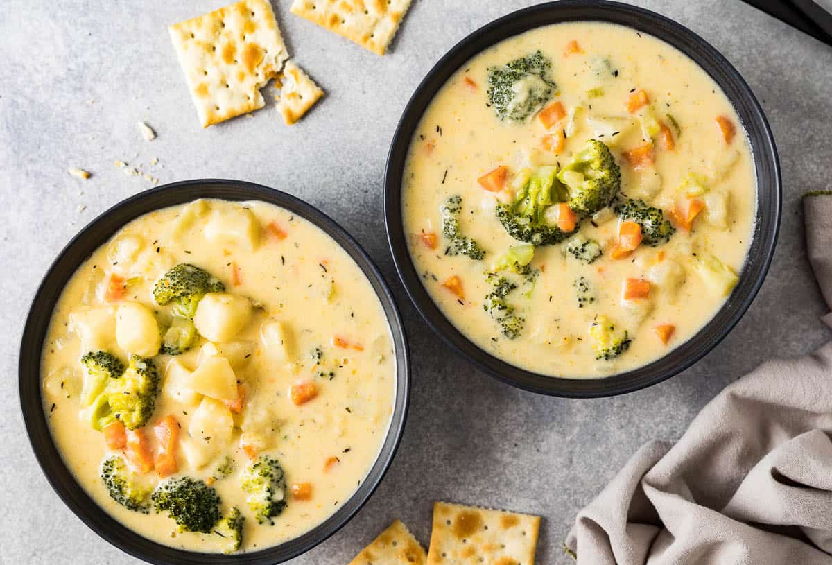 Two bowls of broccoli soup with cheese and potatoes.