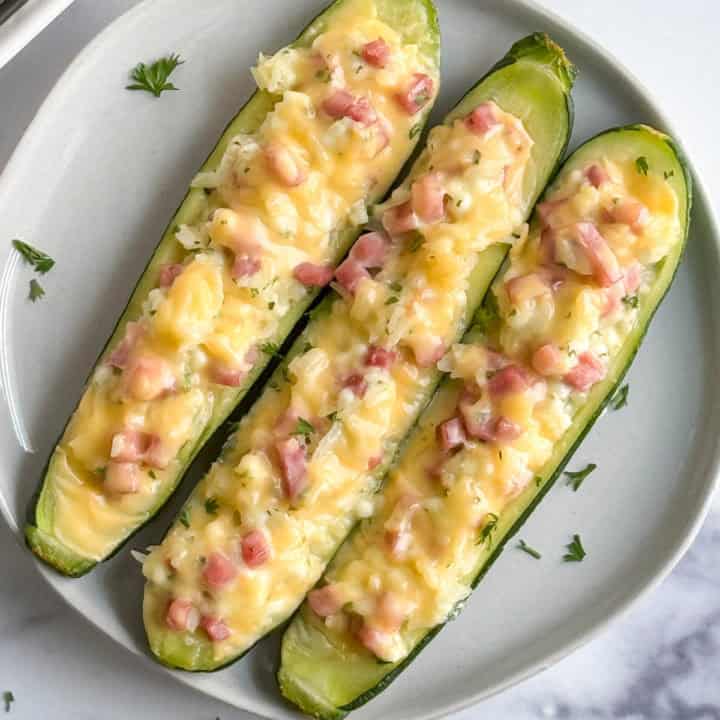 Top down view of ham and cheese stuffed zucchini on a white plate.