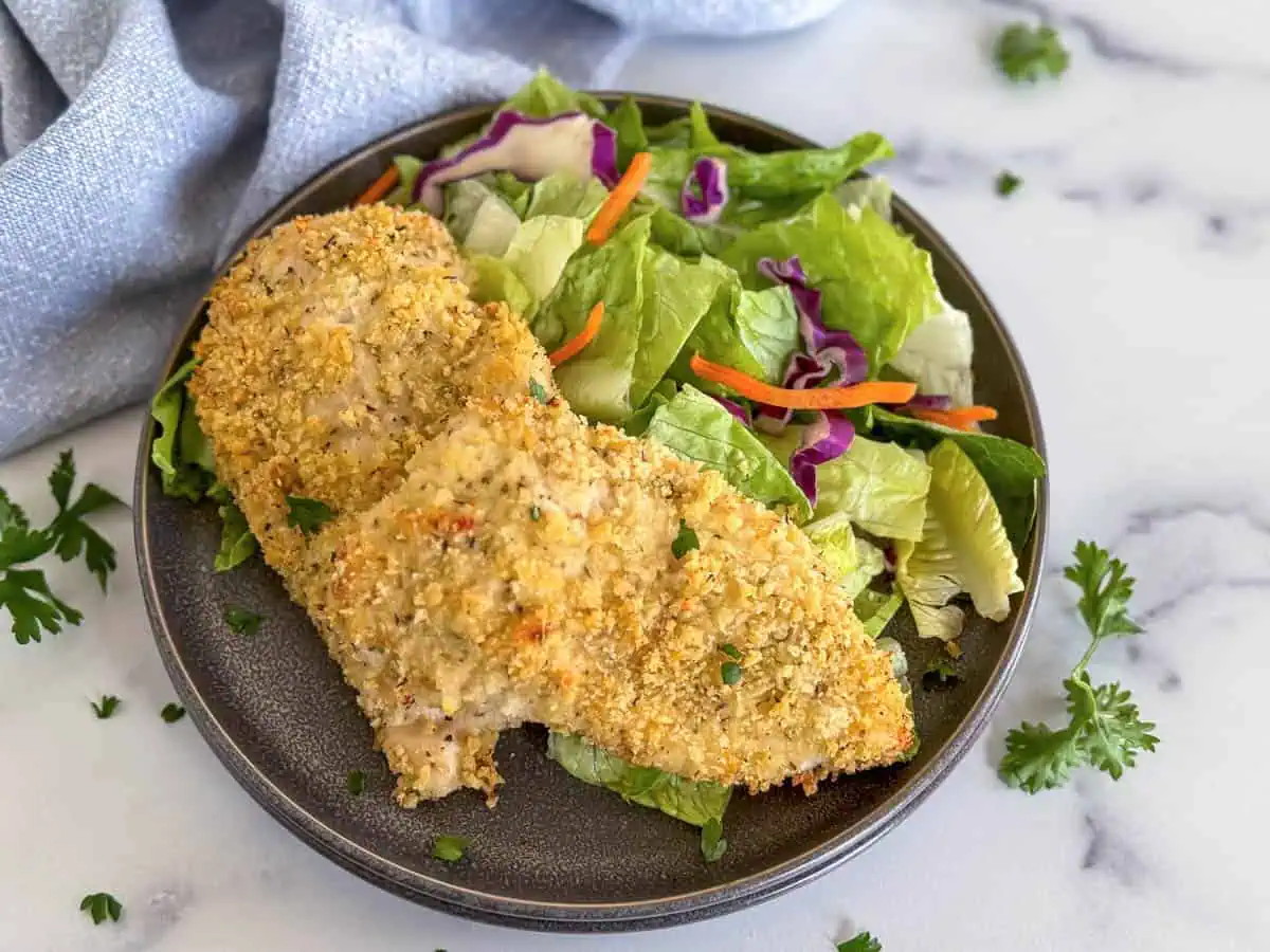 Two baked chicken breasts with panko on a stack of plates.