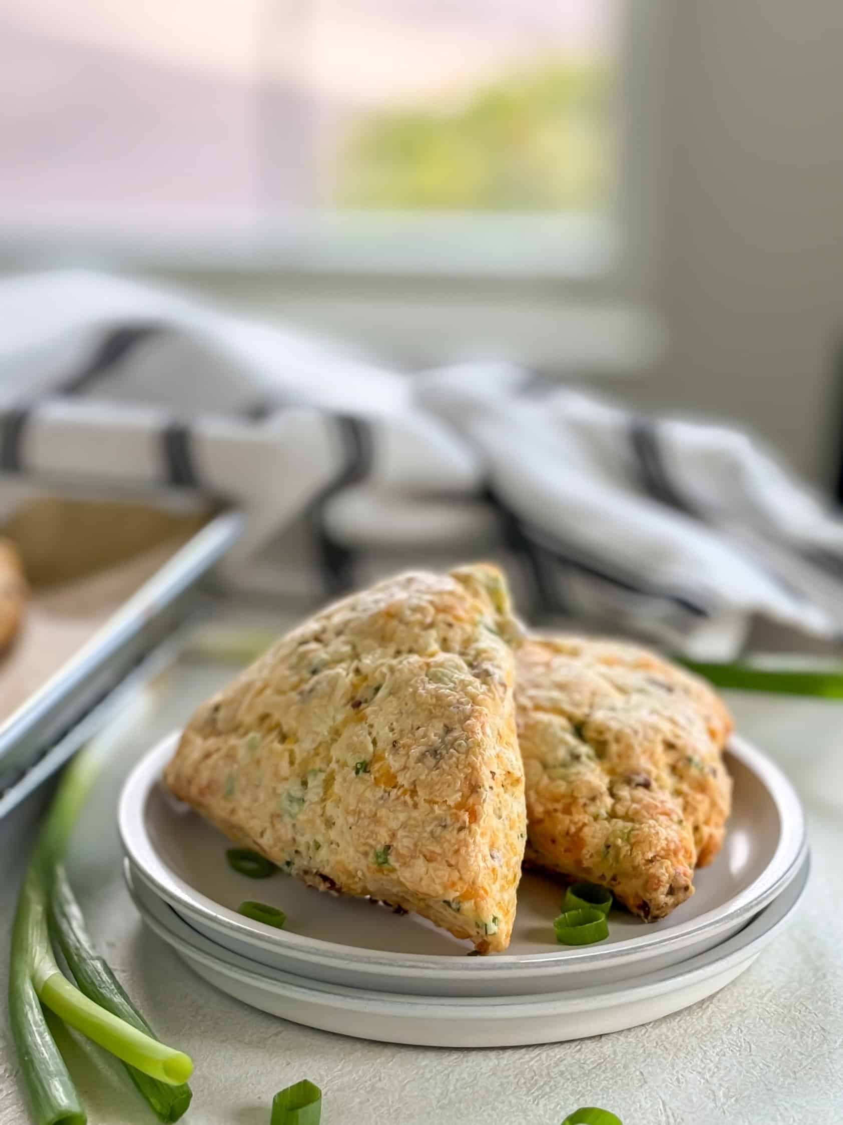 Side view of bacon cheddar scones on a baking tray, with a blurred background of a kitchen setting.