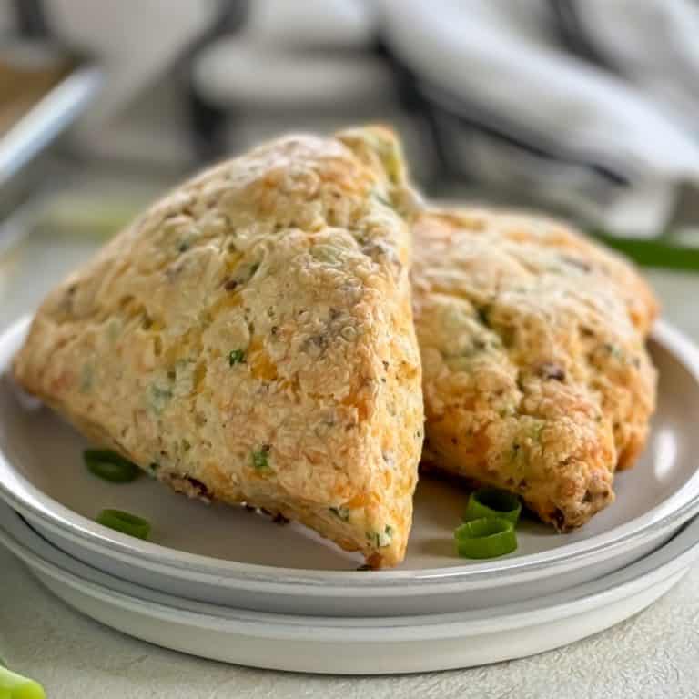 Two bacon cheddar scones on a white plate garnished with green onion slices.