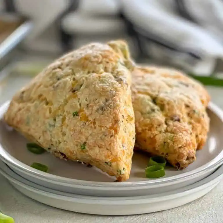 Two bacon cheddar scones on a white plate garnished with green onion slices.