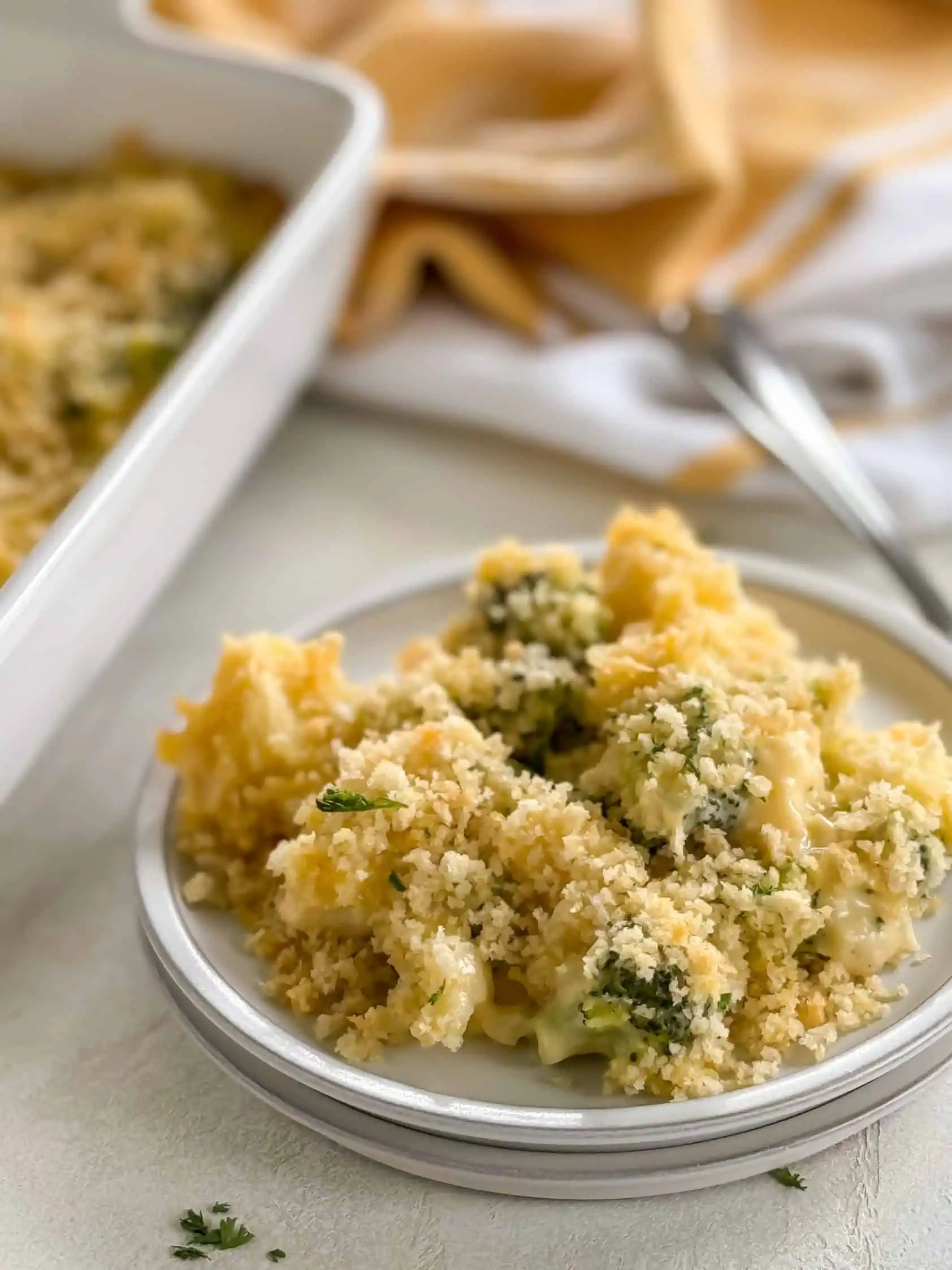 A close-up of a serving of creamy broccoli and cauliflower casserole with a golden breadcrumb topping on a white plate.