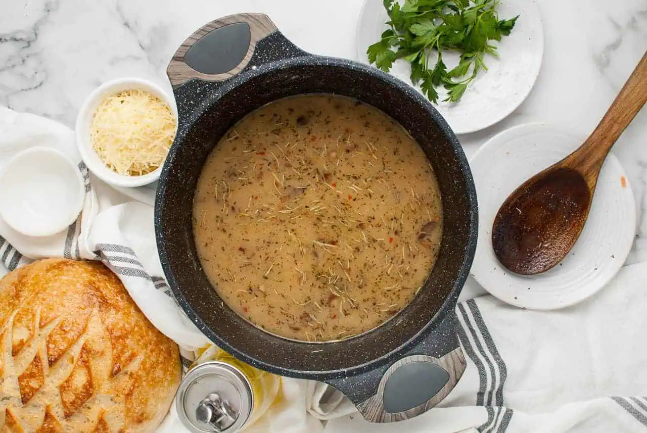 A pot of simmering broth and vegetables with grated parmesan cheese and fresh parsley on the side.