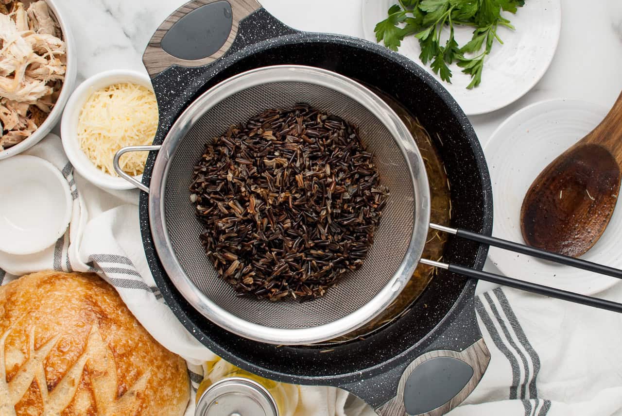 A strainer filled with cooked wild rice placed over a pot of broth.