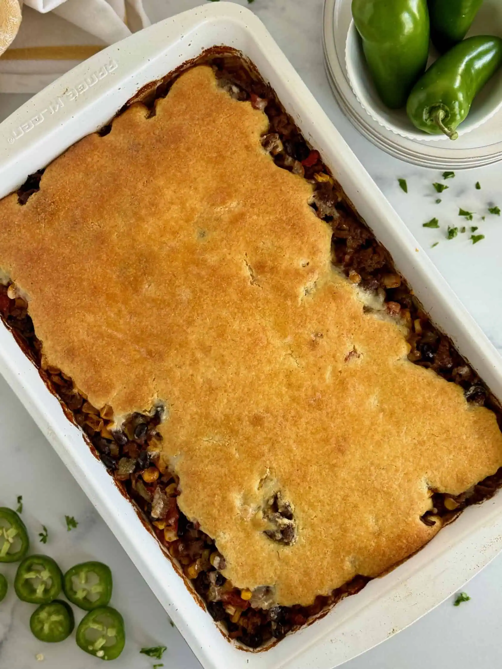 A top view of a 9x13-inch baking dish filled with hamburger cornbread casserole, with a golden cornbread crust.