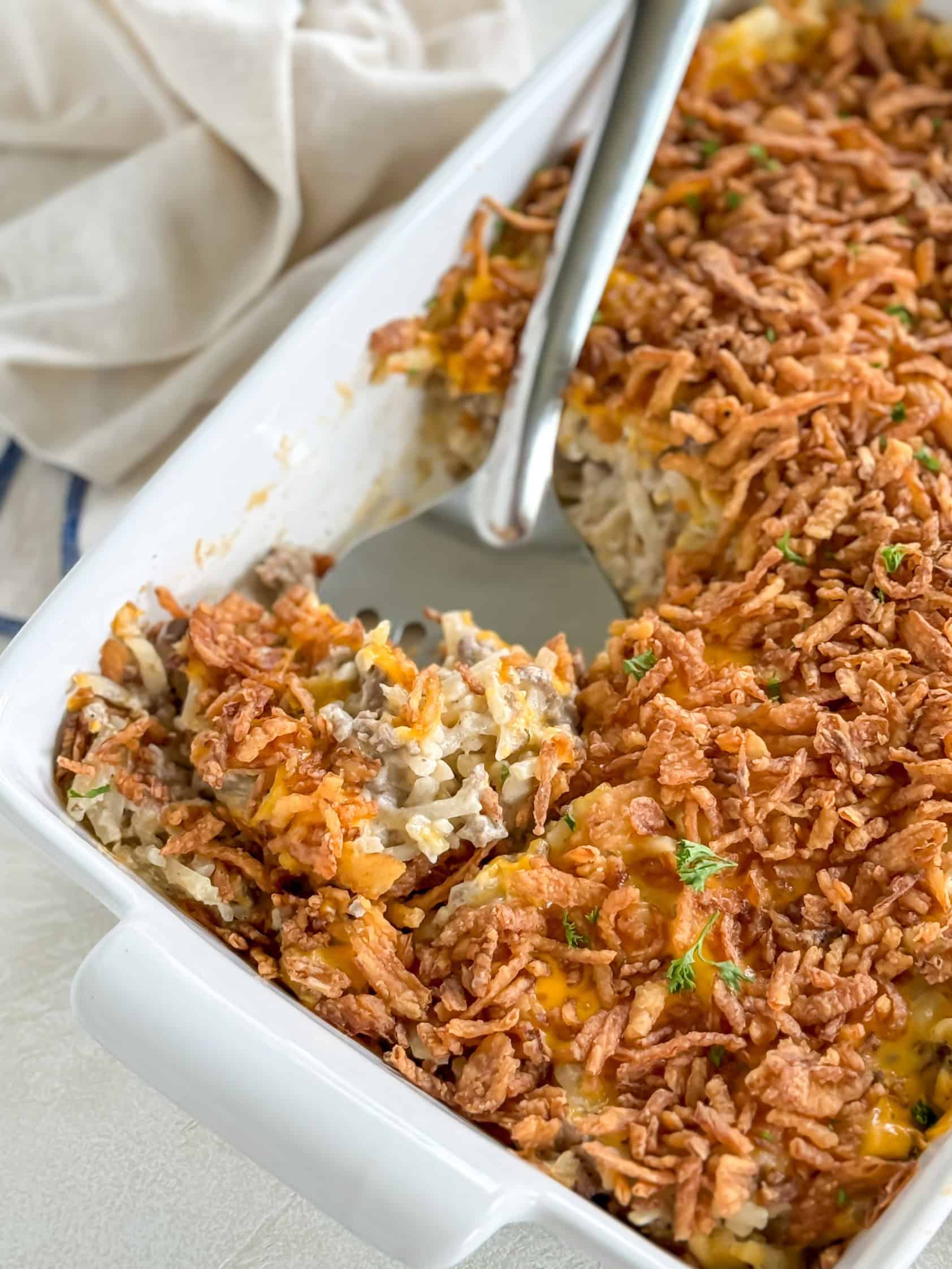 Hamburger hashbrown casserole with a portion scooped out, revealing the savory ground beef and hashbrown filling.