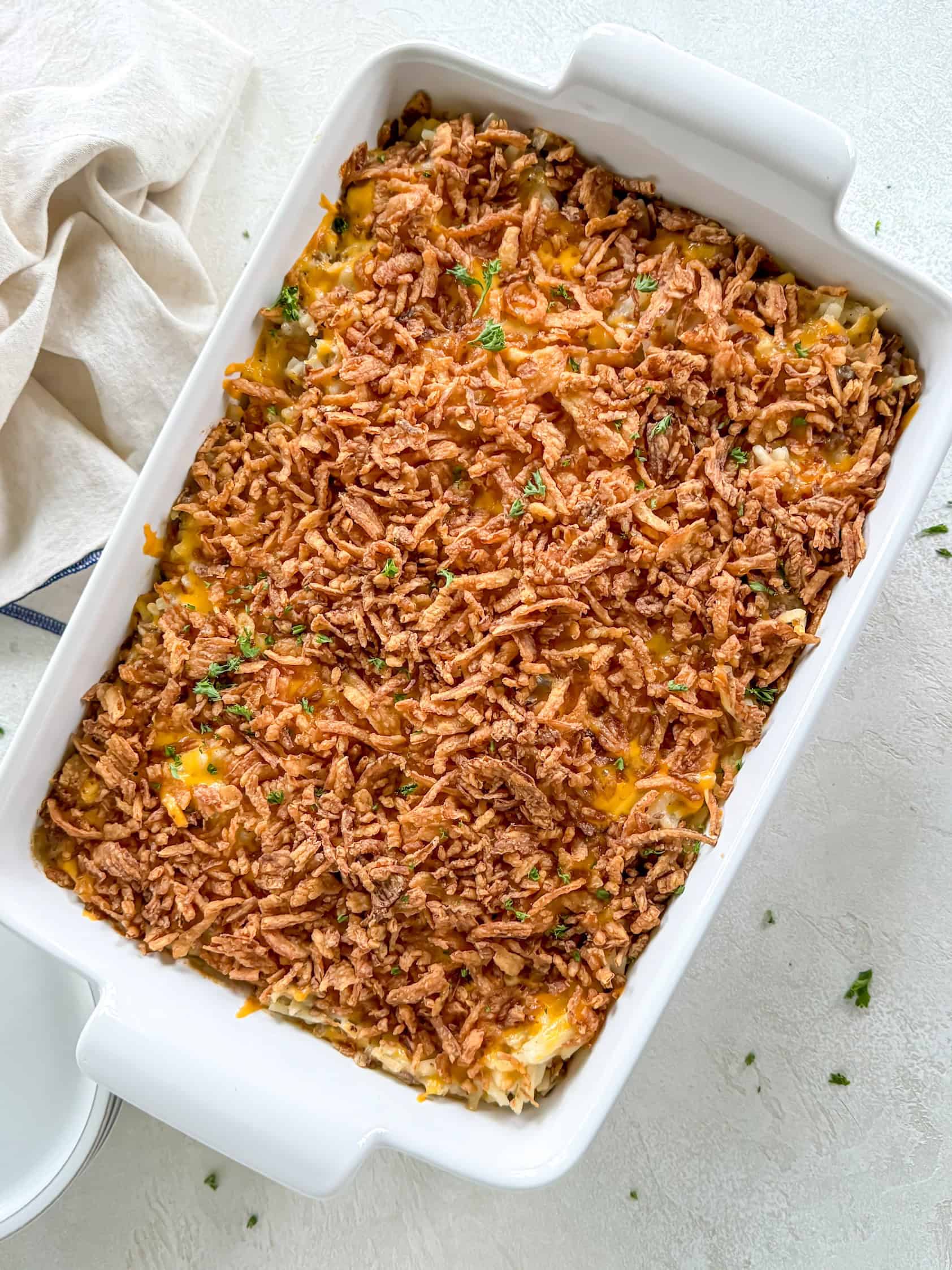 A freshly baked hamburger hashbrown casserole topped with crispy french fried onions in a white baking dish.