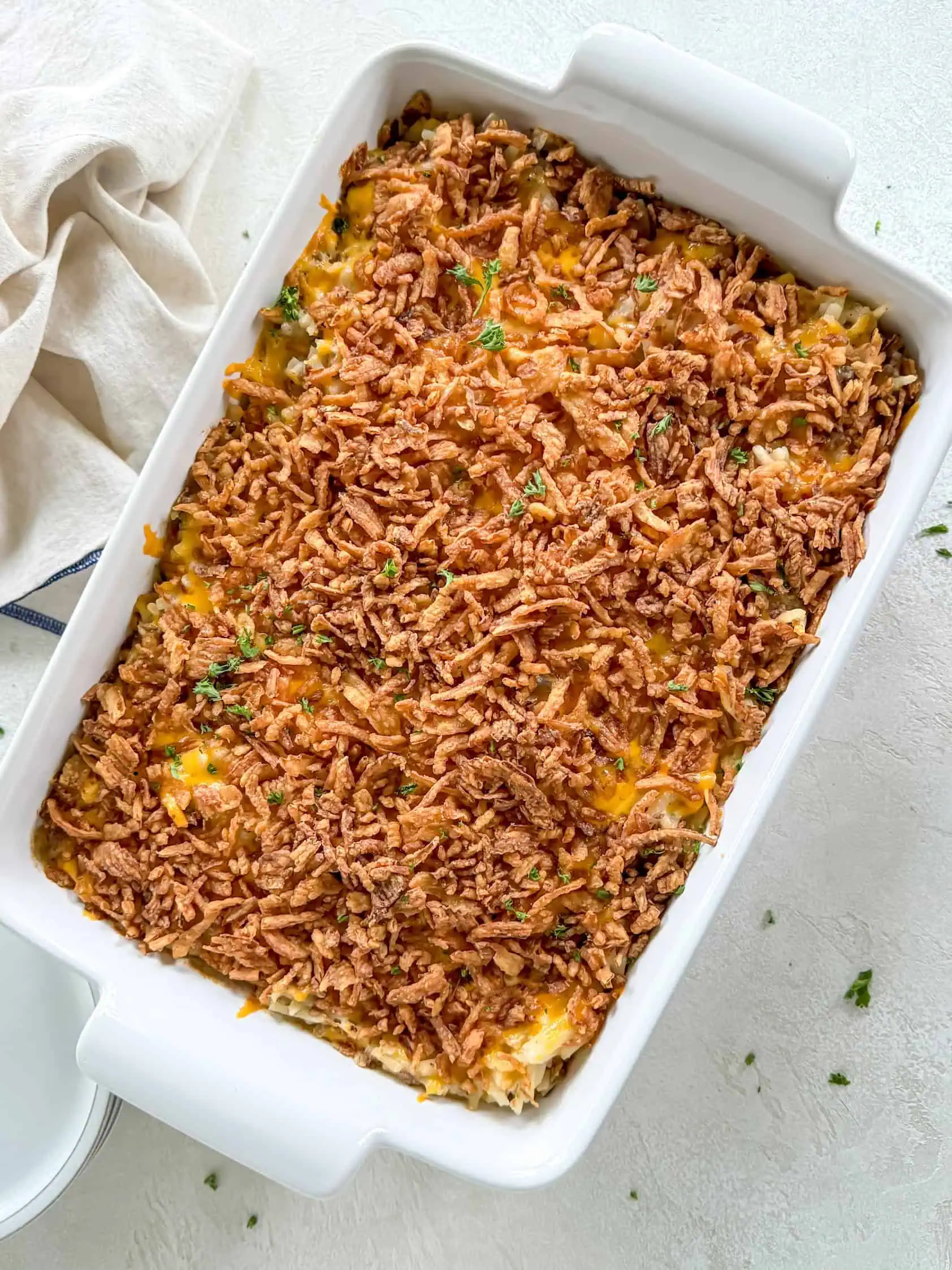 A freshly baked hamburger hashbrown casserole topped with crispy french fried onions in a white baking dish.