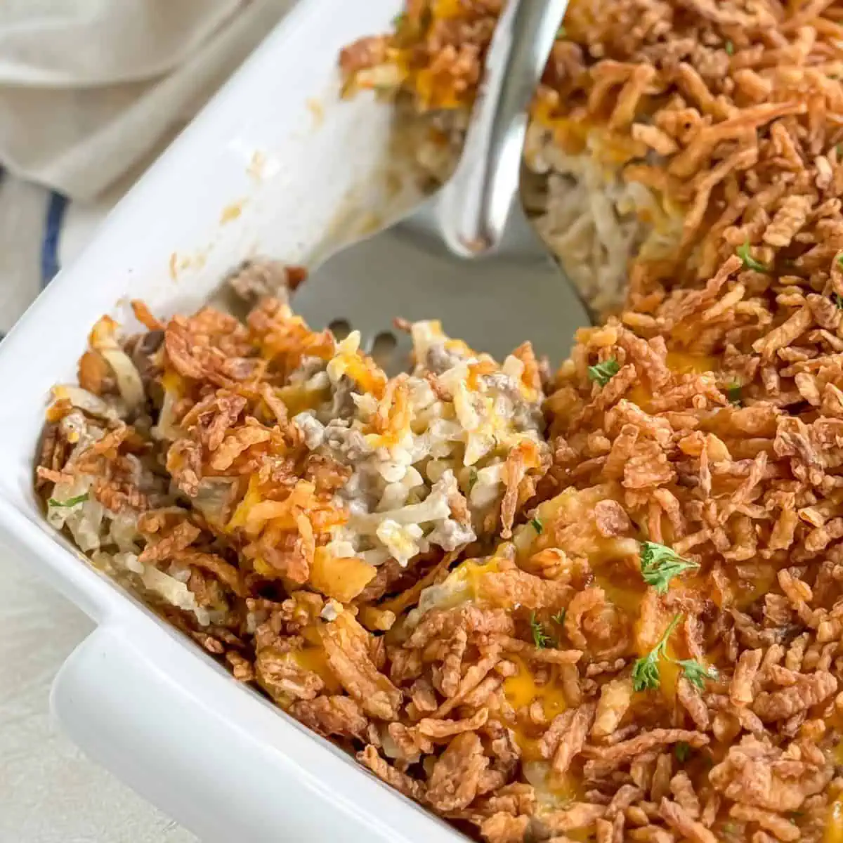 Close-up of hamburger hashbrown casserole with a serving spoon, showcasing the golden-brown crispy topping and cheesy layers.