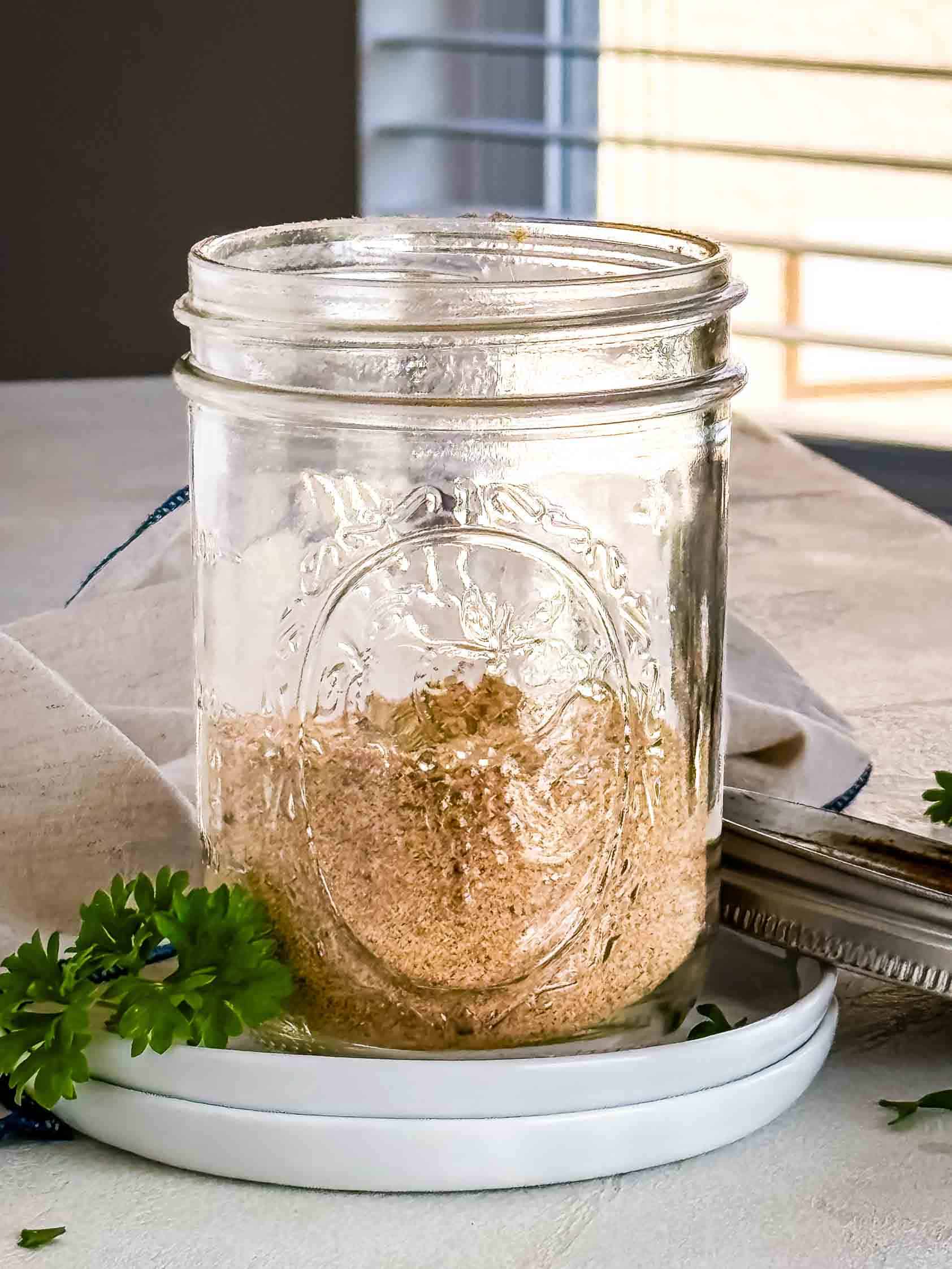 A close-up of homemade seasoned salt in a glass mason jar, with parsley and a cloth napkin nearby.
