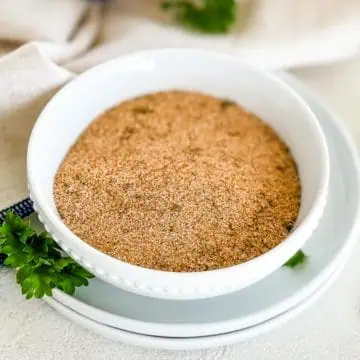 A white bowl filled with homemade seasoned salt, garnished with fresh parsley, on a white plate.