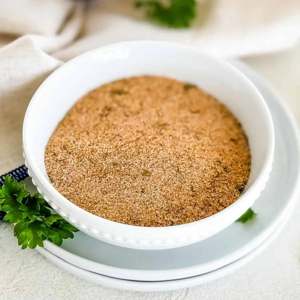 A white bowl filled with homemade seasoned salt, garnished with fresh parsley, on a white plate.