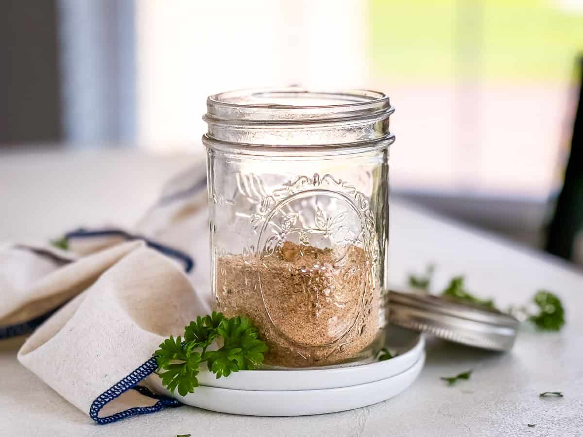 Homemade seasoned salt in a glass mason jar, with fresh parsley and a cloth napkin in the background.