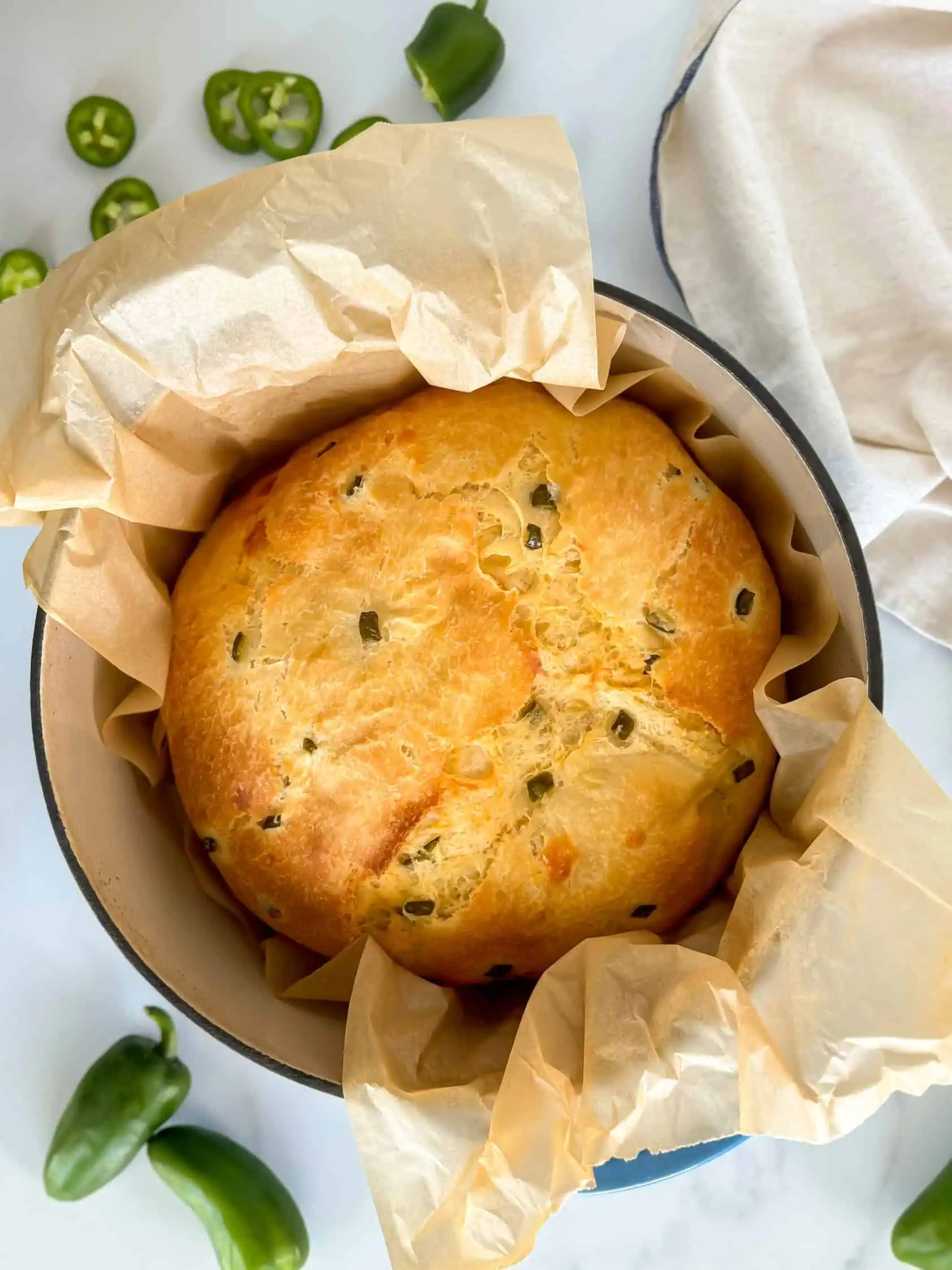 Close-up of a whole loaf of bread in a parchment-lined dutch oven, showcasing a golden-brown crust.