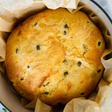 Whole loaf of freshly baked bread in a parchment-lined dutch oven.