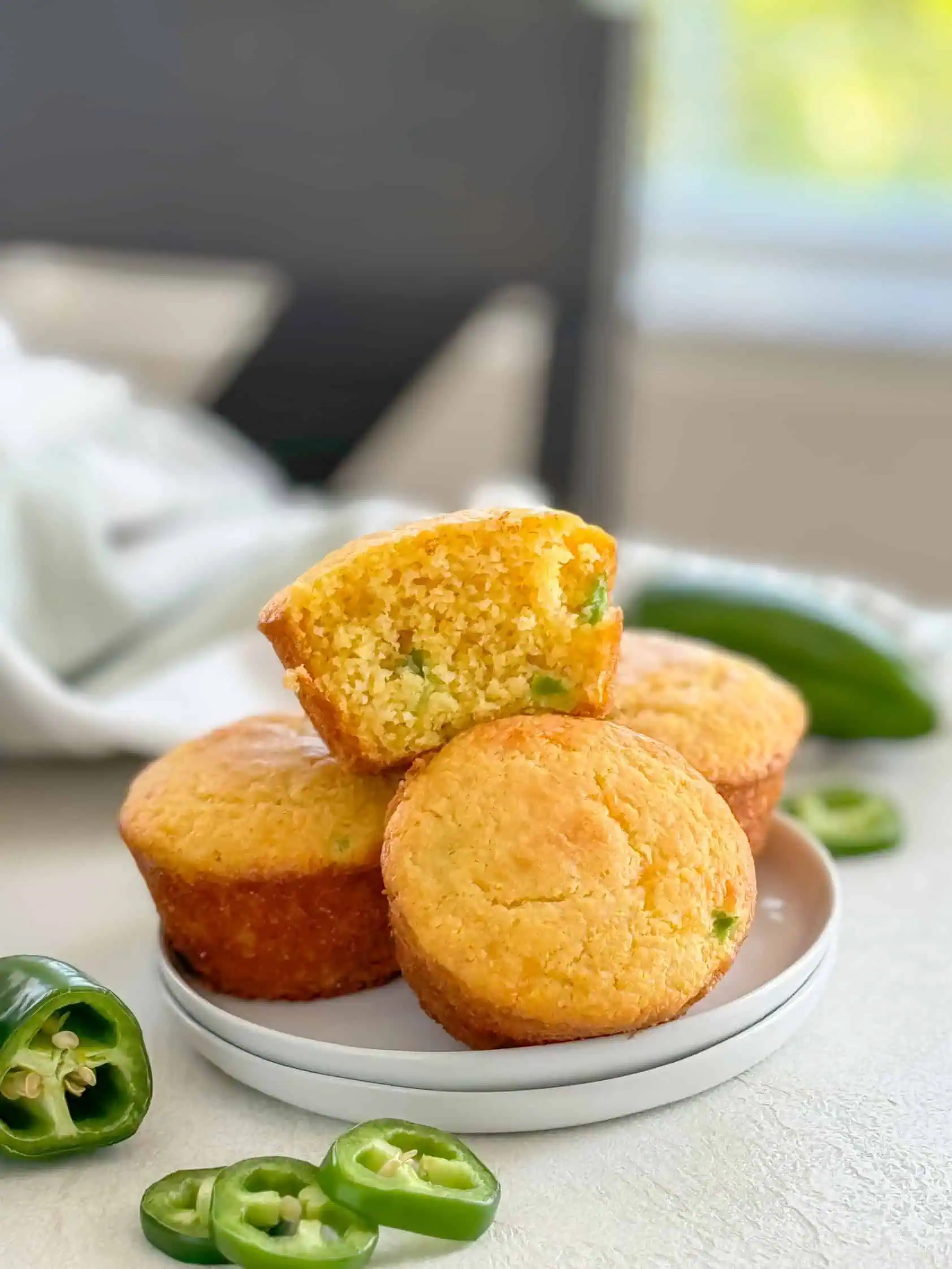 Cheesy jalapeño cornbread muffins on a plate with fresh jalapeño slices in the foreground.