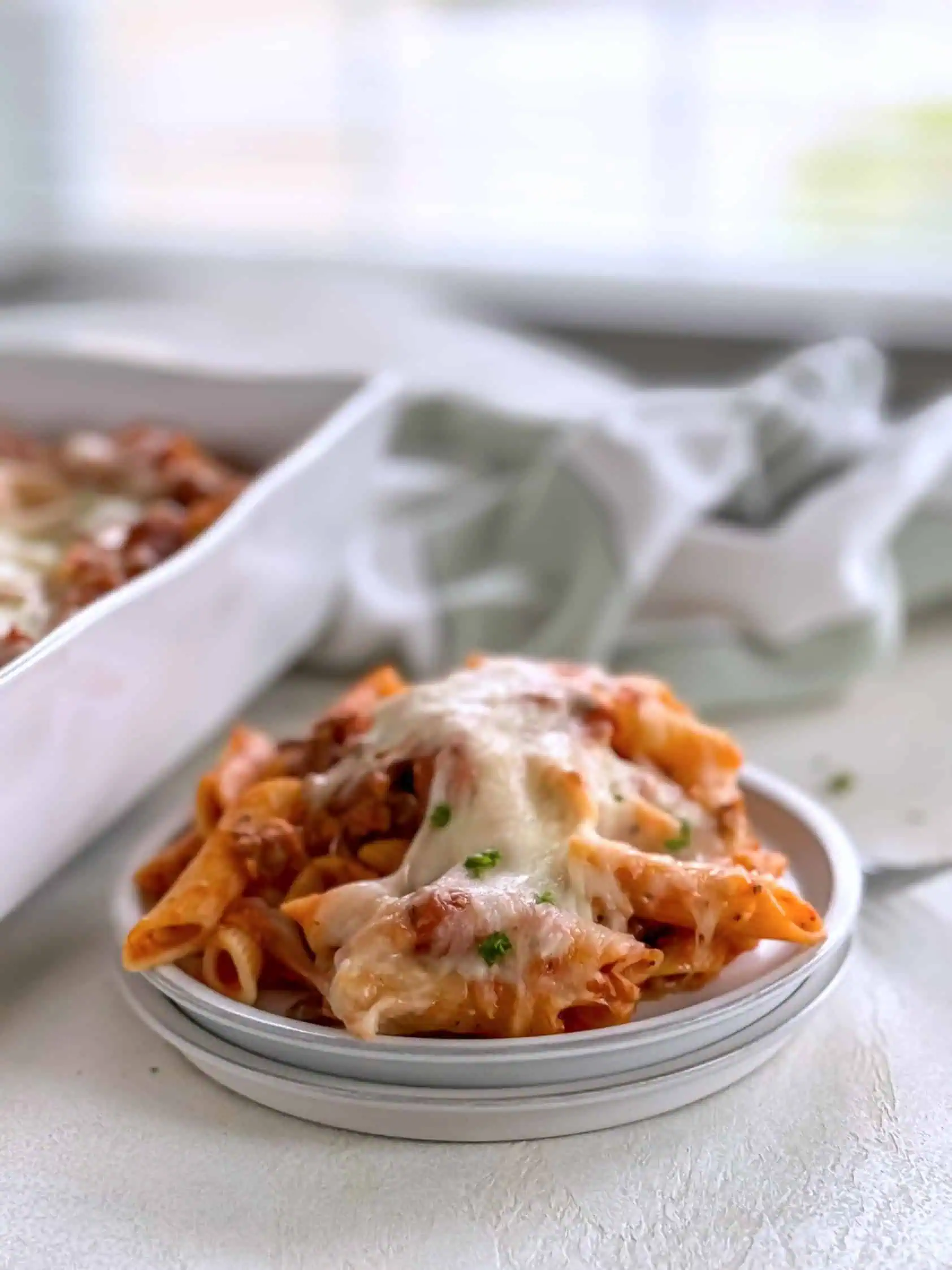 A close-up shot of a plate of cheesy baked penne pasta with sausage and marinara sauce, showing the rich, melted cheese on top.