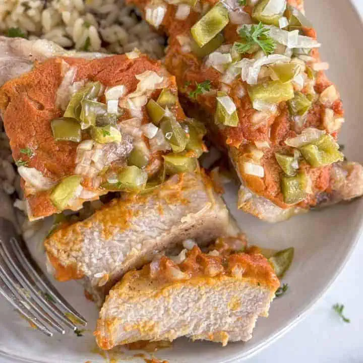 Close-up of tender smothered pork chop with a fork, topped with peppers and onions.