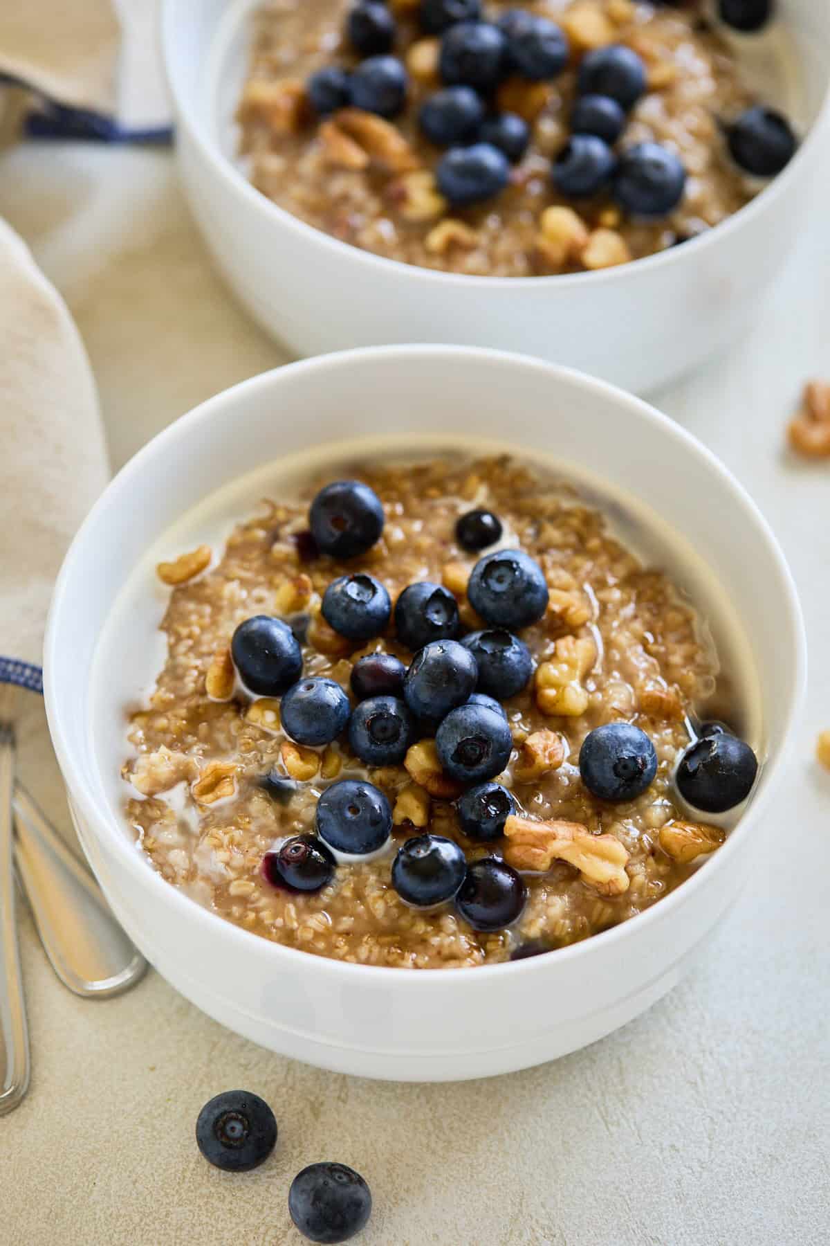 Steel cut oats with fresh blueberries and walnuts served in a white bowl, with a drizzle of milk.