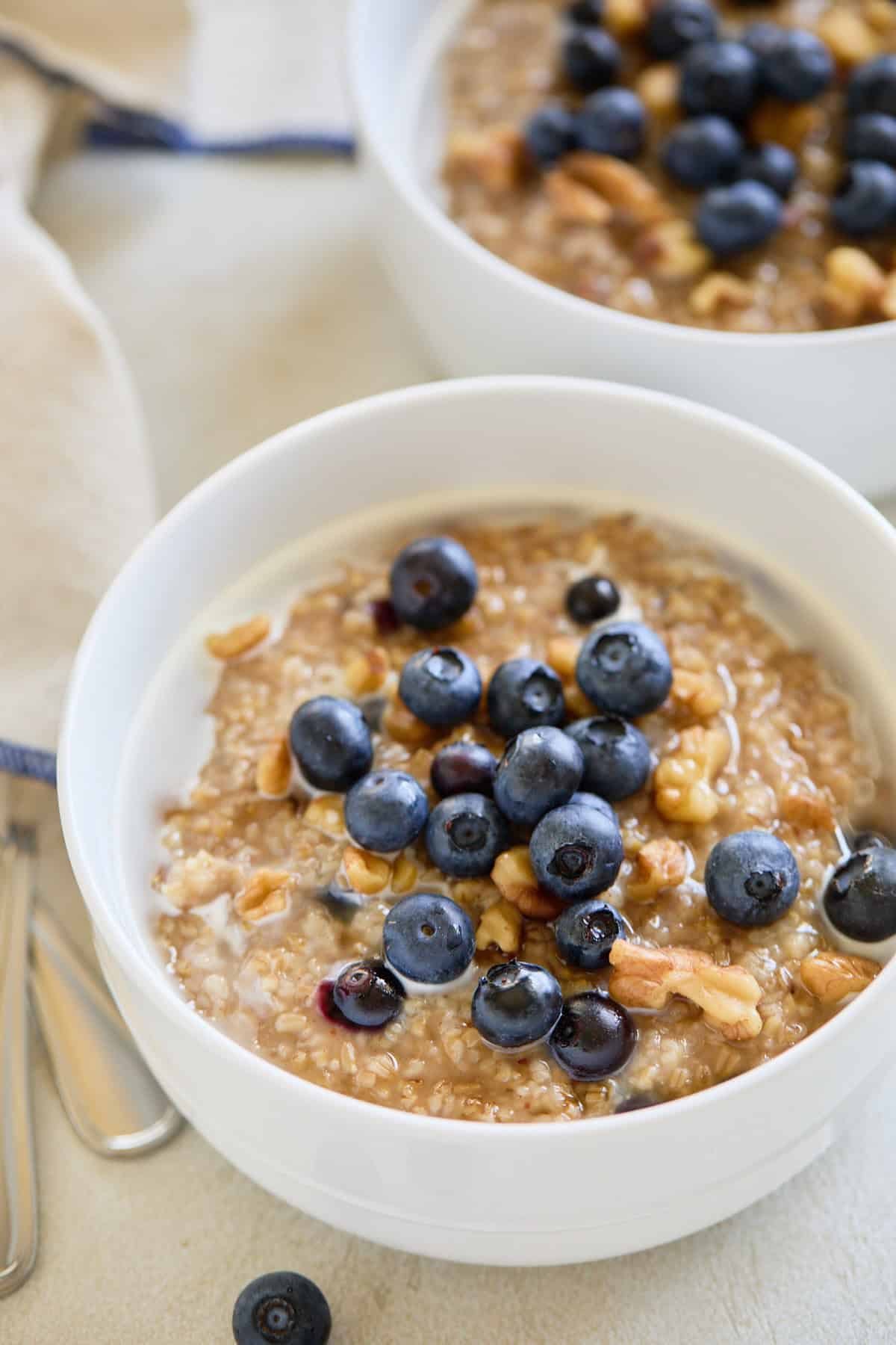 Two bowls of cooked steel cut oats topped with fresh blueberries and walnuts, ready to serve.