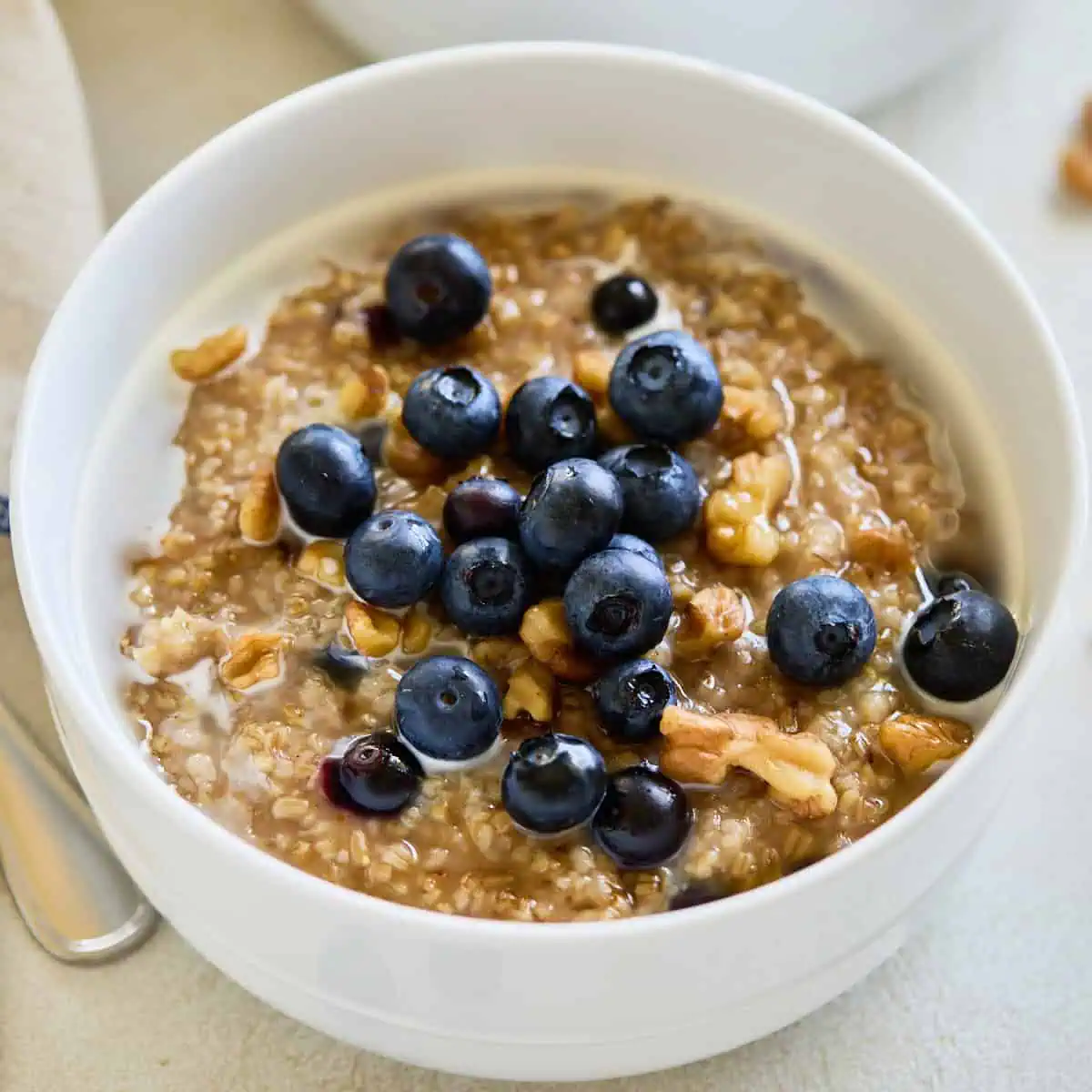 Two bowls of cooked steel cut oats topped with fresh blueberries and walnuts, ready to serve.