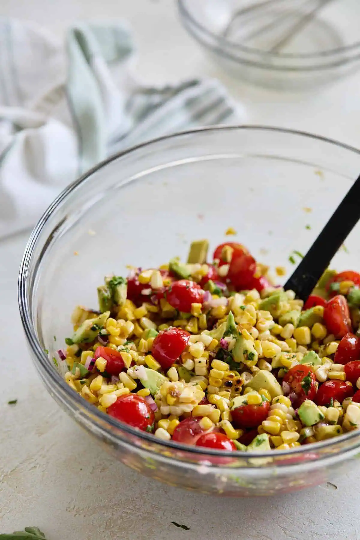 A glass bowl filled with the mixed salad ingredients, with a whisk in the background.