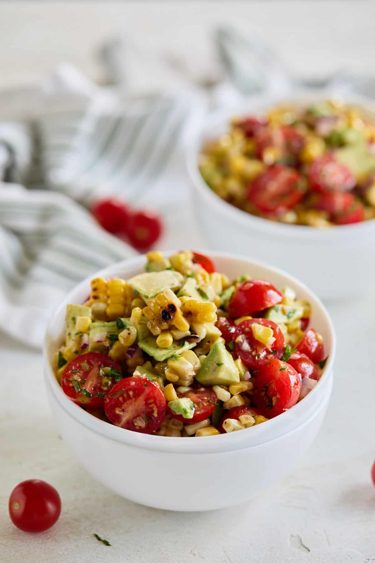 Two bowls of the salad on a light-colored surface with a striped towel and cherry tomatoes in the background.