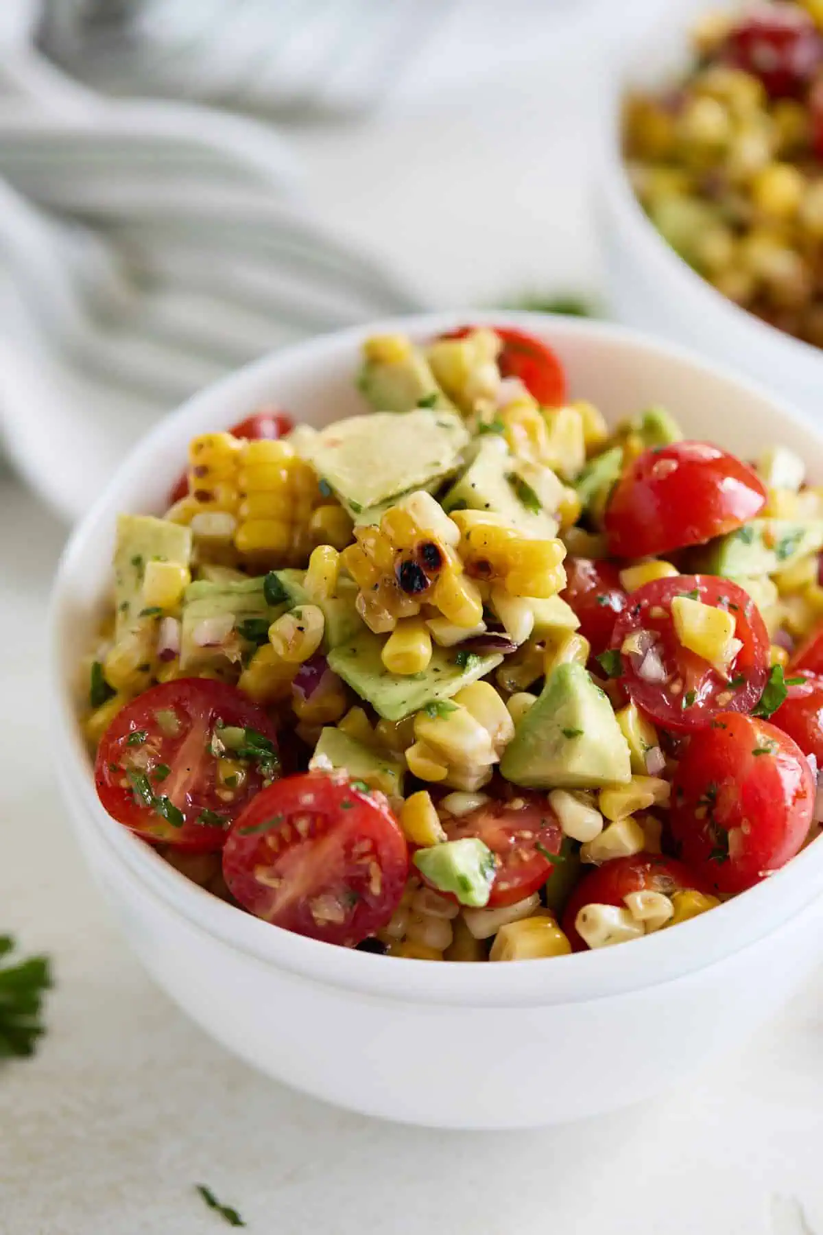 A close-up view of corn tomato avocado salad in a white bowl, focusing on the vibrant colors and textures of the ingredients.