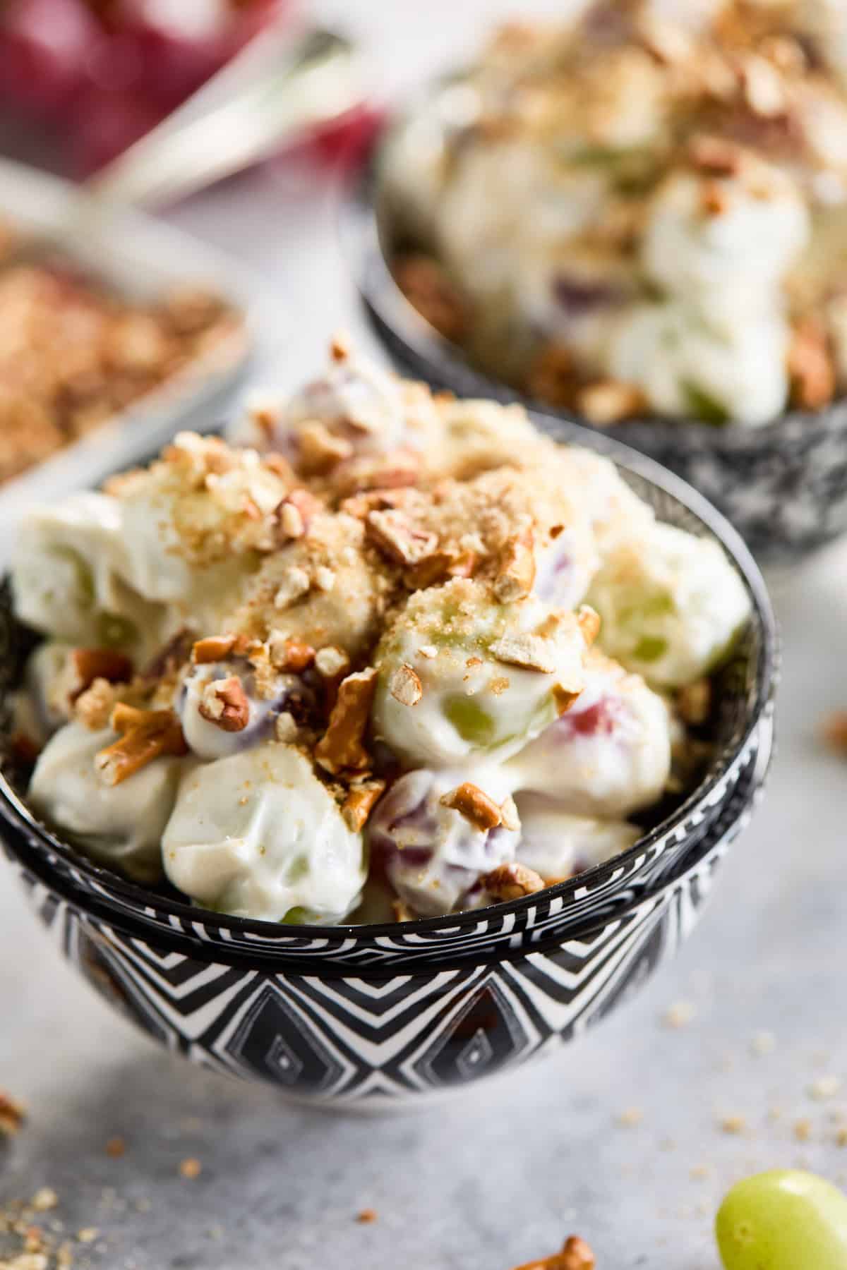 Two servings of grape salad with a crunchy topping, with fresh grapes and additional topping in the background.