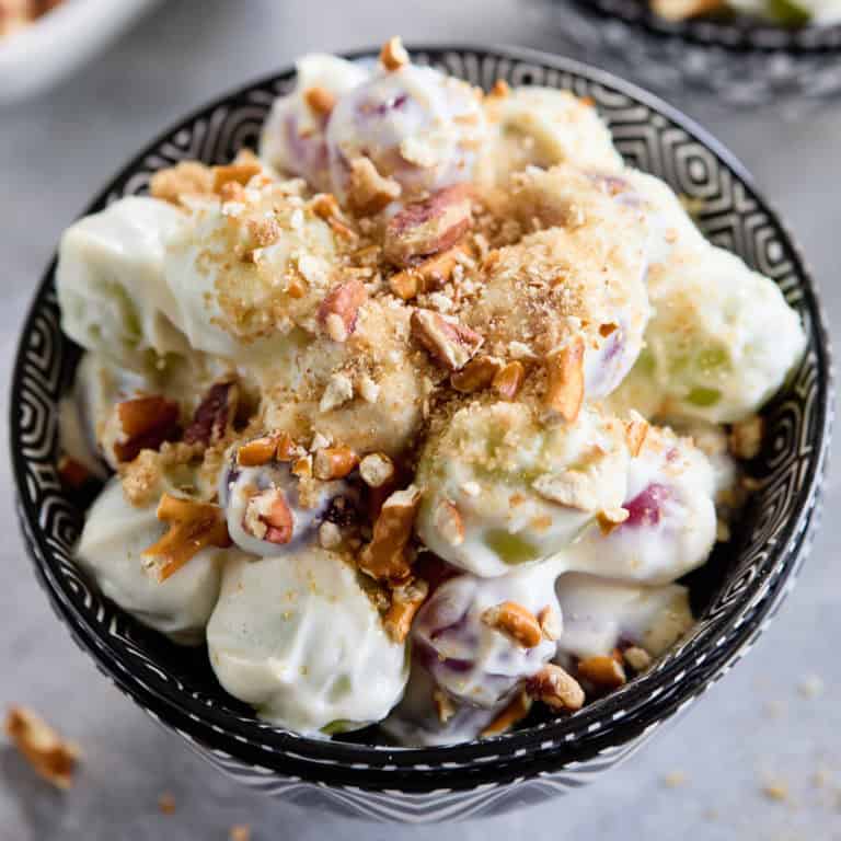 A bowl of grape salad topped with chopped pecans and crushed pretzels.