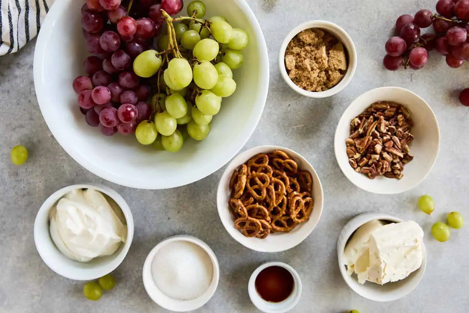 A bowl of mixed green and red grapes with ingredients for grape salad arranged around it.